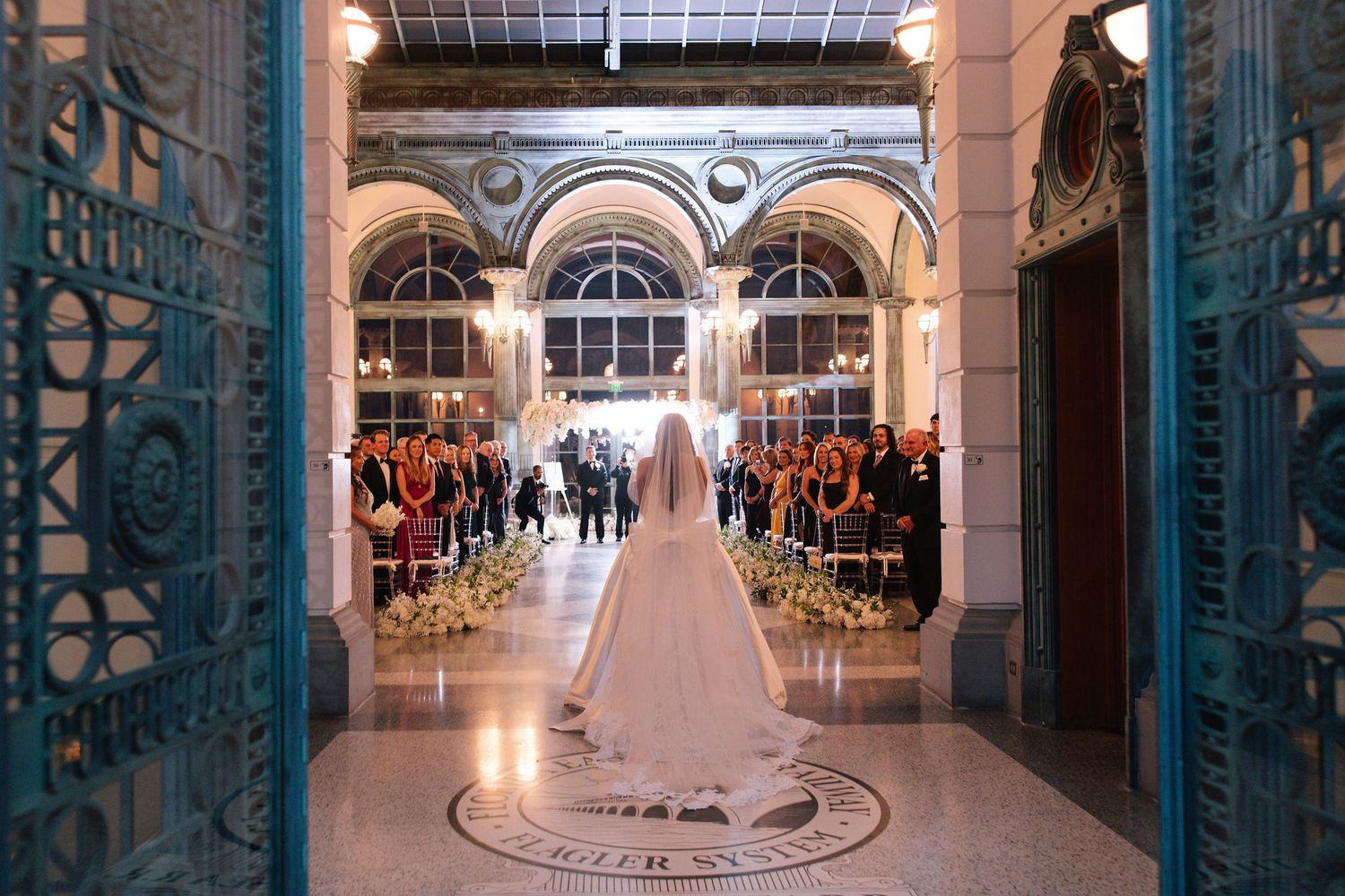 Grand hallway with ornate blue doors and white wedding dress display in luxurious venue.