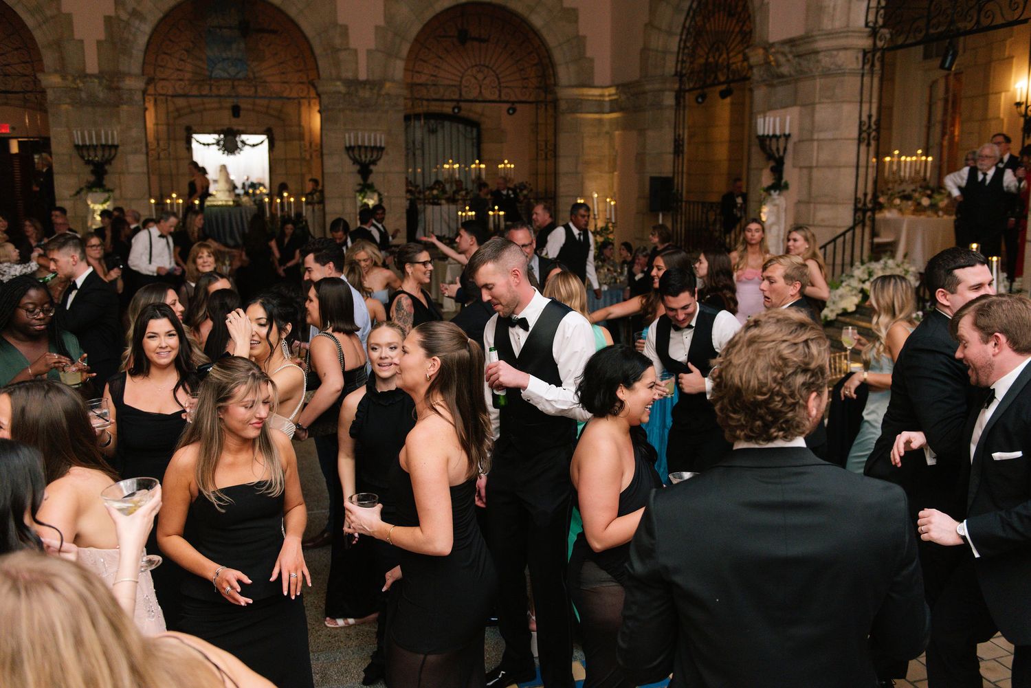 Wedding reception guests dancing and celebrating in an elegant ballroom with arched architecture.