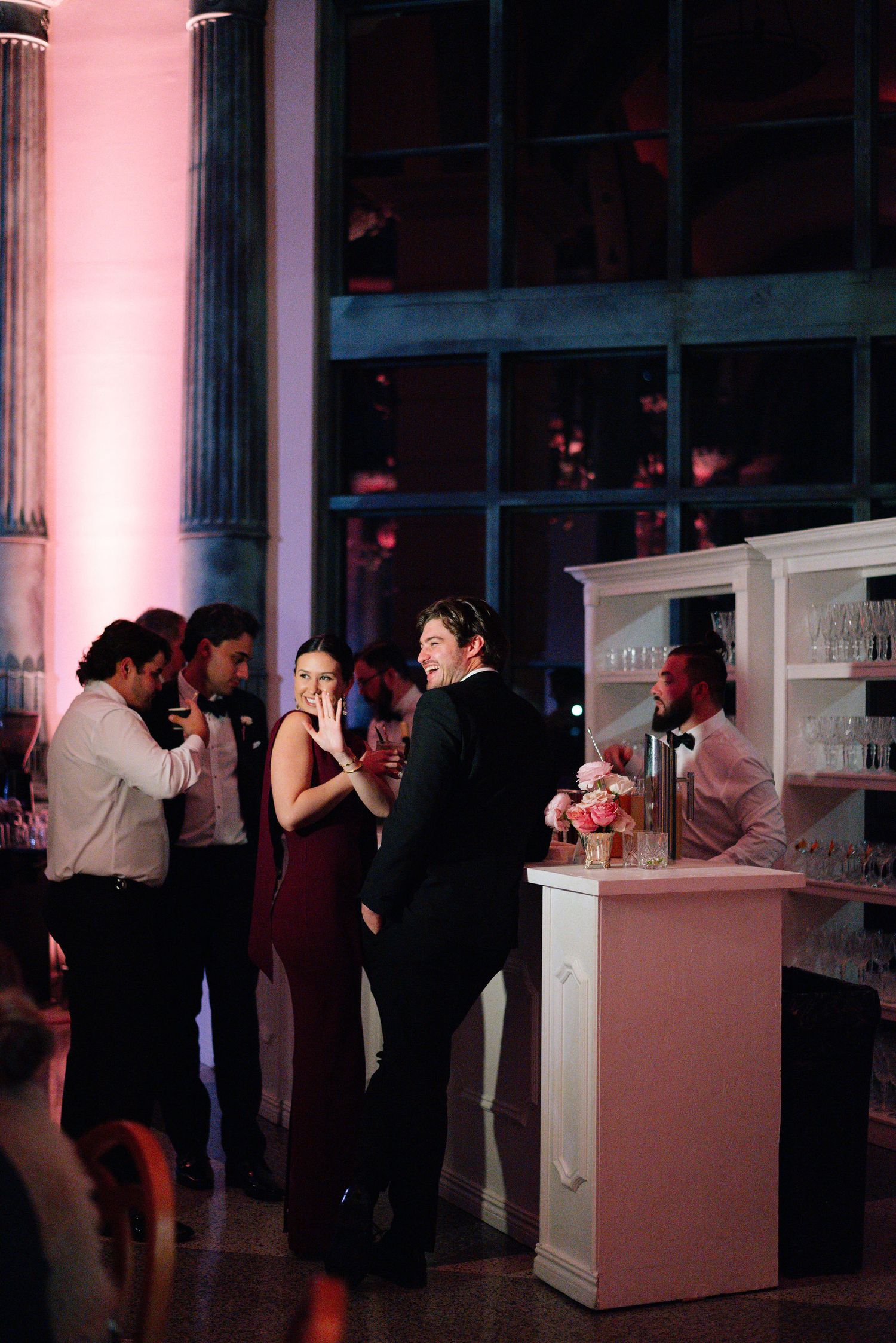 Wedding reception guests mingling at illuminated bar stations with pink ambient lighting.