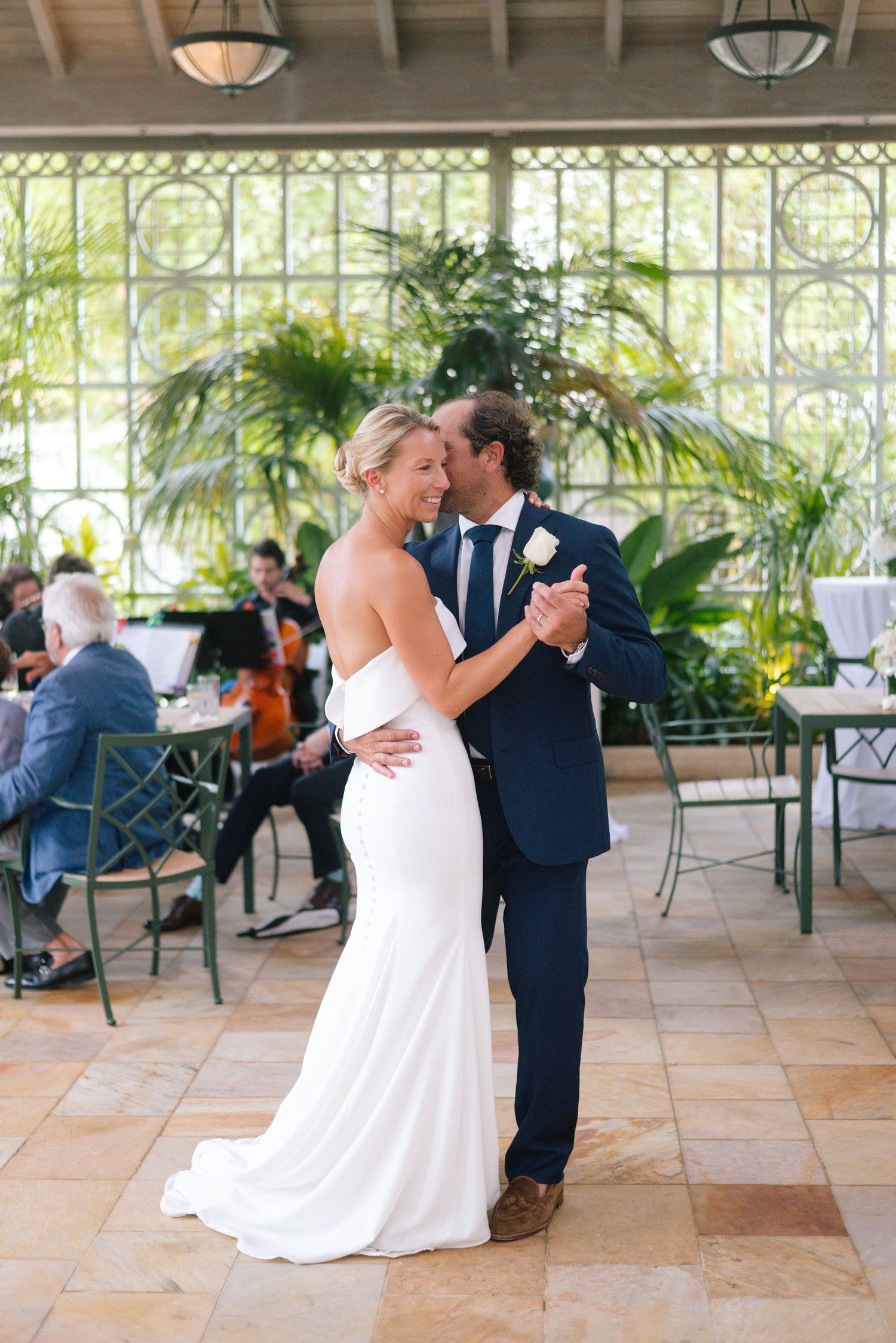 Couple sharing their first dance in an elegant conservatory with floor-to-ceiling windows.