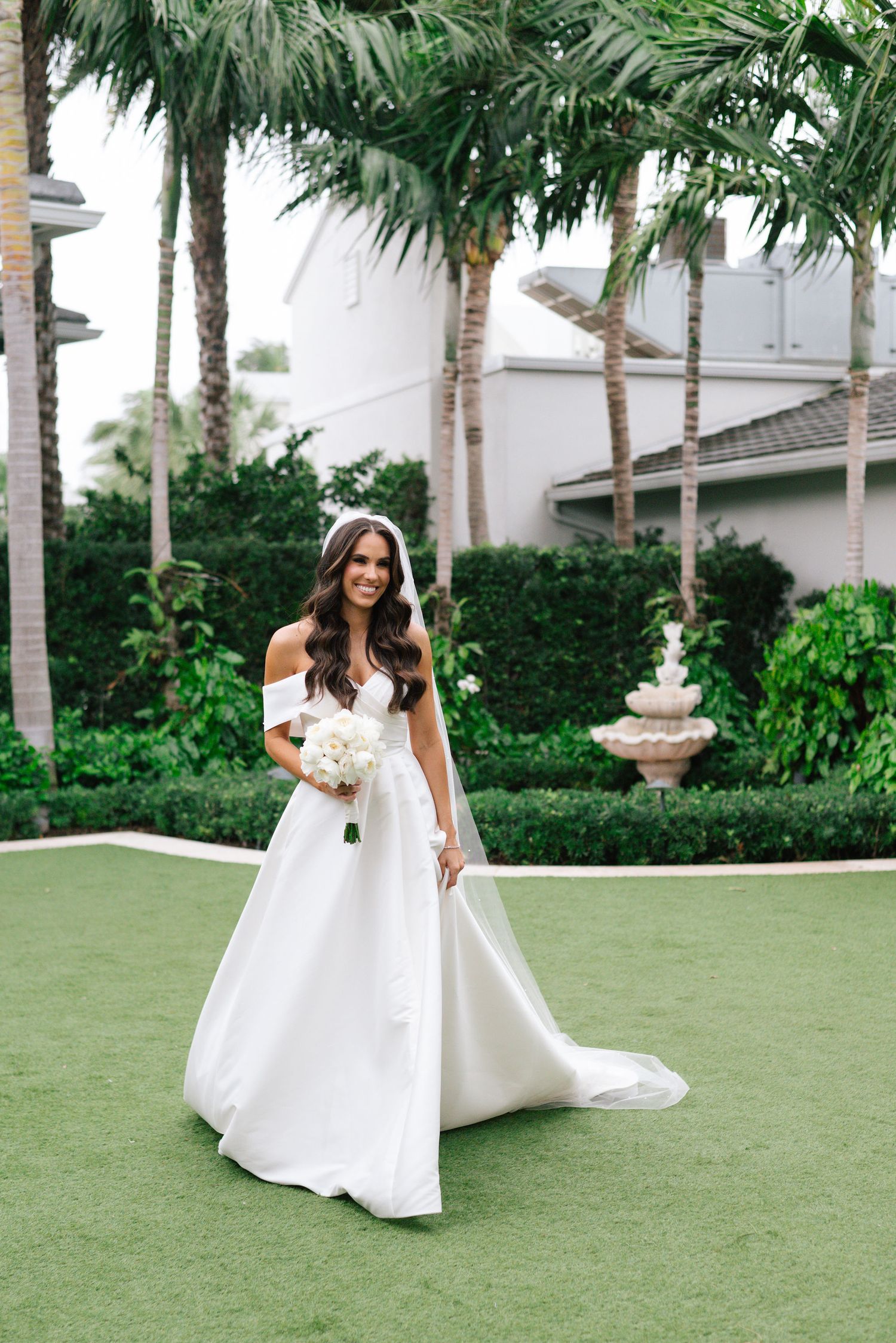 An elegant bridal portrait session on a manicured lawn surrounded by palm trees.