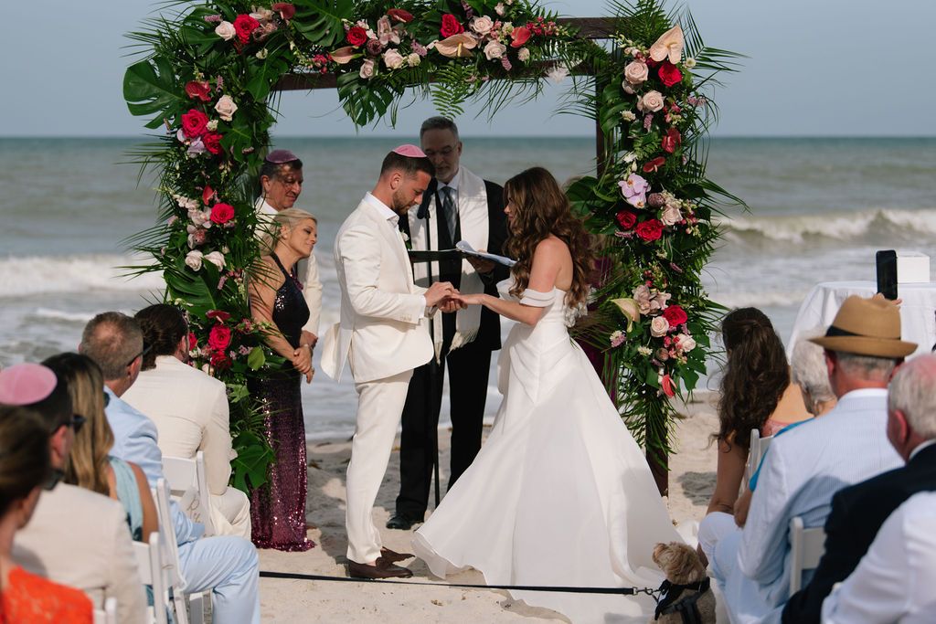 Wedding ceremony moments captured under tropical floral arch on beach.