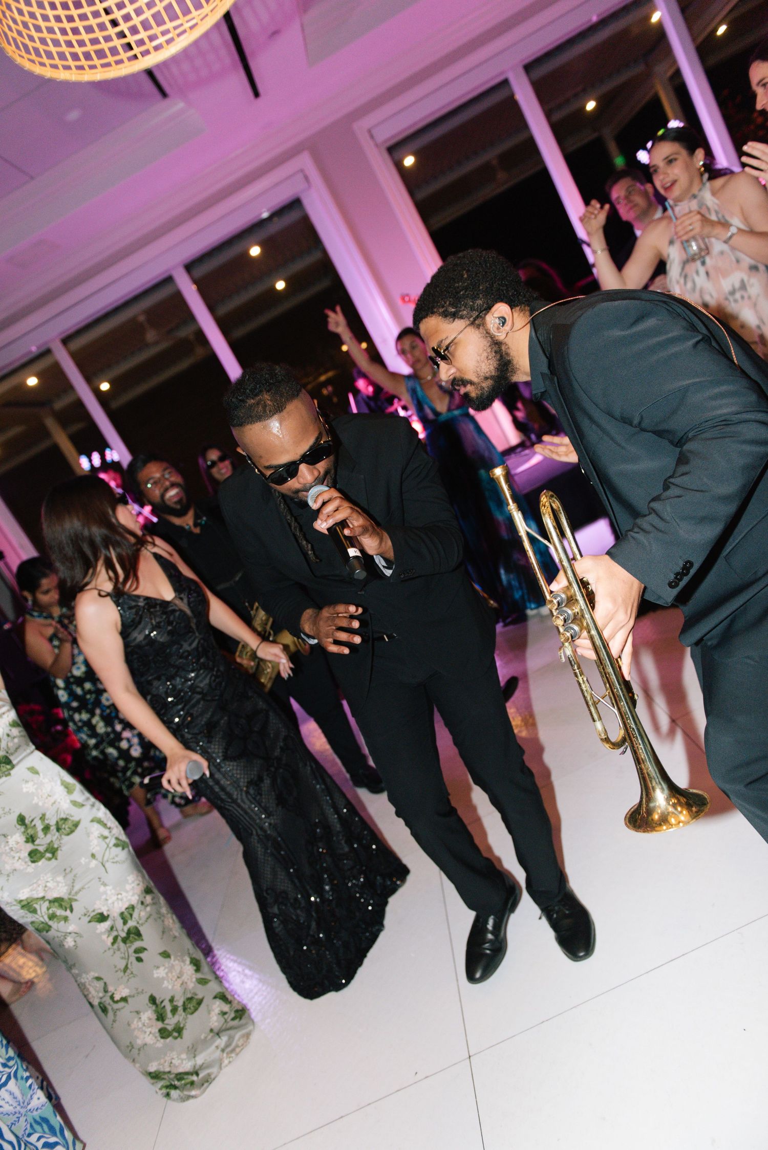 Wedding reception dance party with musicians playing trumpet in a purple-lit room.