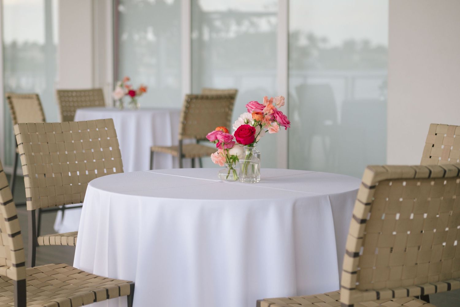 Clean modern reception setup with round tables and tan chairs in a bright venue.