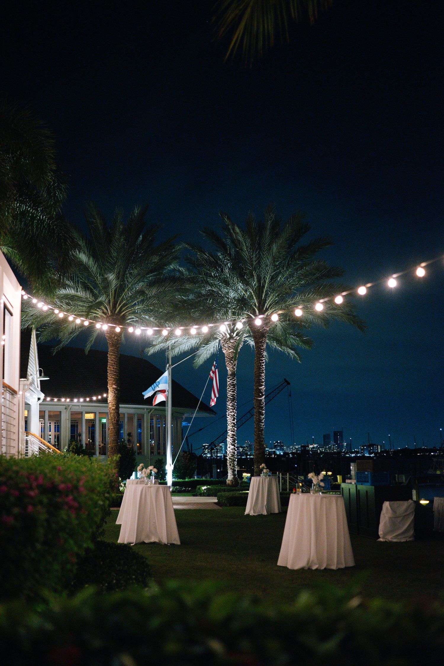Evening wedding reception setup with string lights and palm trees creating a romantic outdoor ambiance.