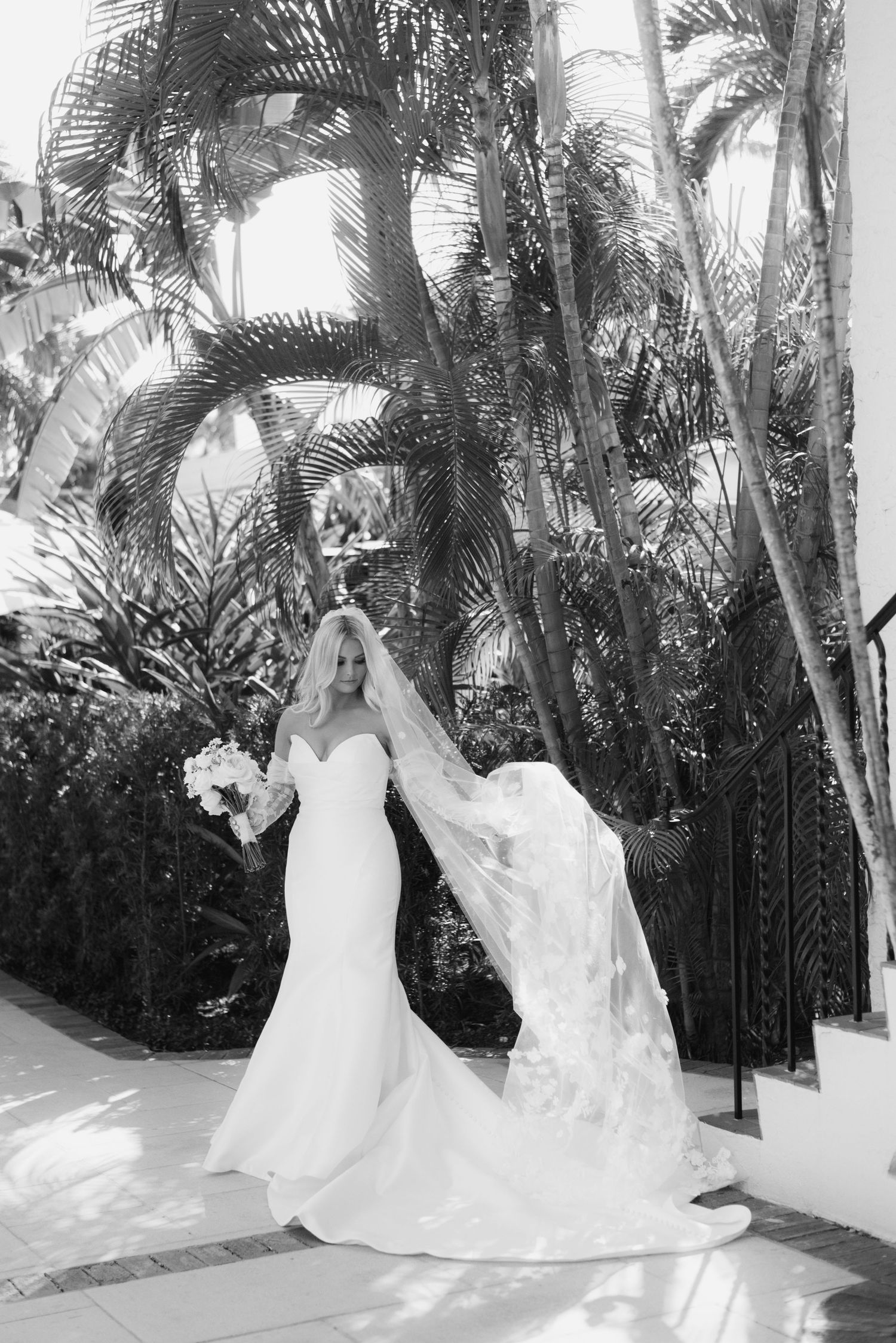 Black and white photos of a wedding dress flowing in the breeze among tropical palm trees.