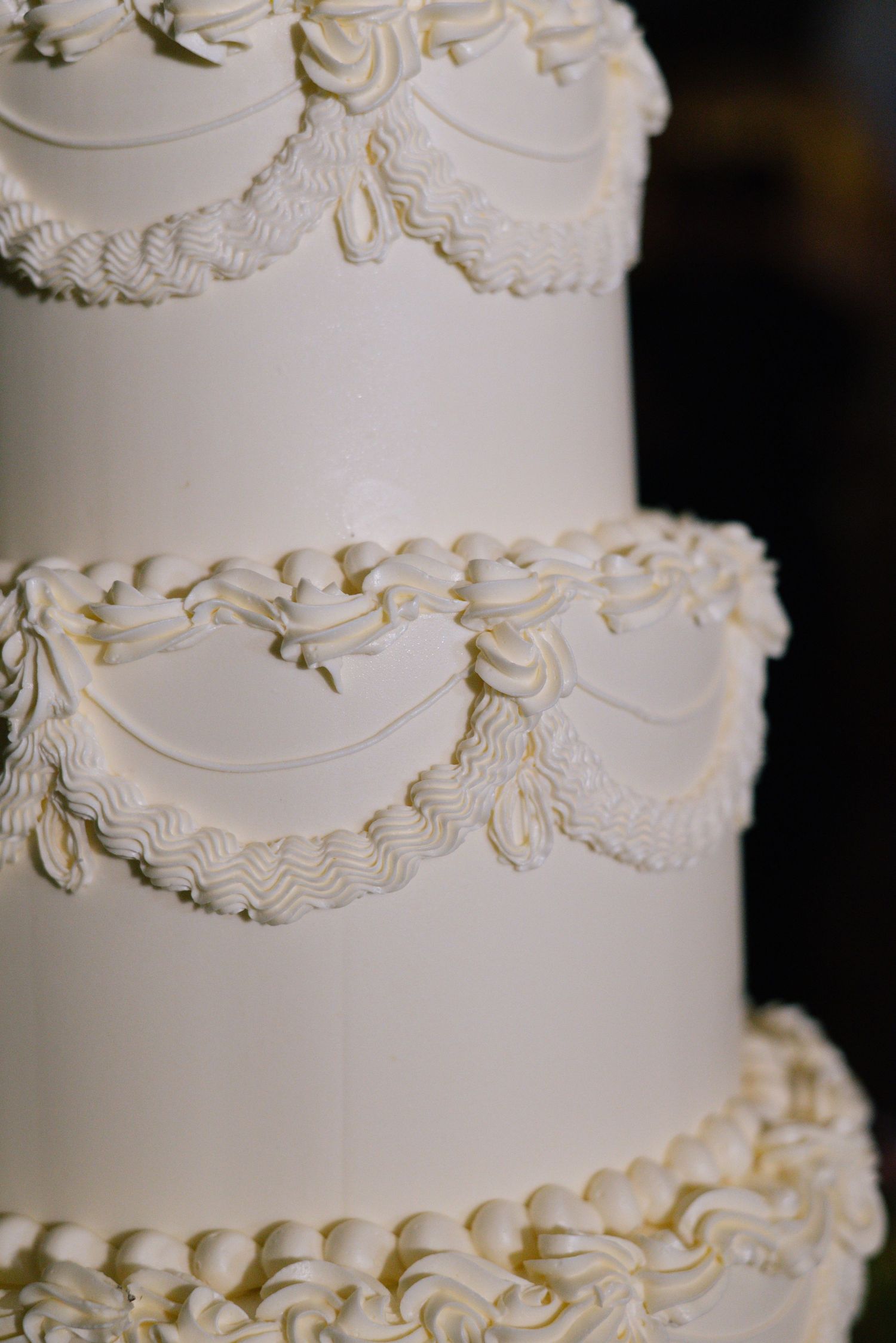 Close-up detail of a white wedding cake with intricate piped frosting decorations and delicate floral patterns.