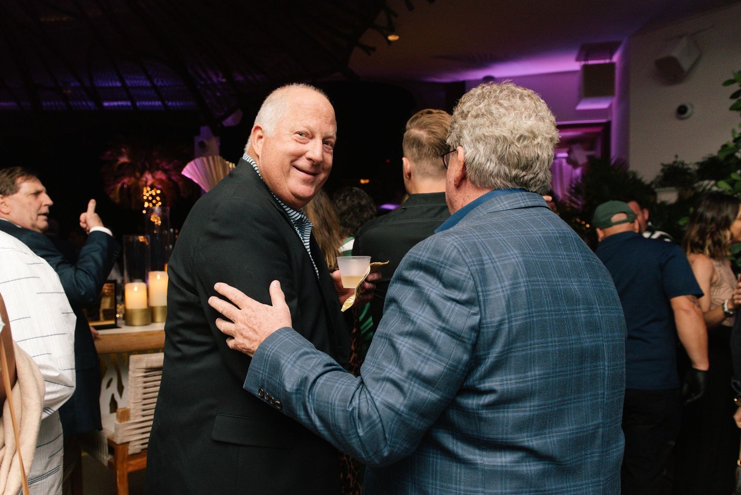 People mingling and socializing at a dimly lit evening event with purple ambient lighting.