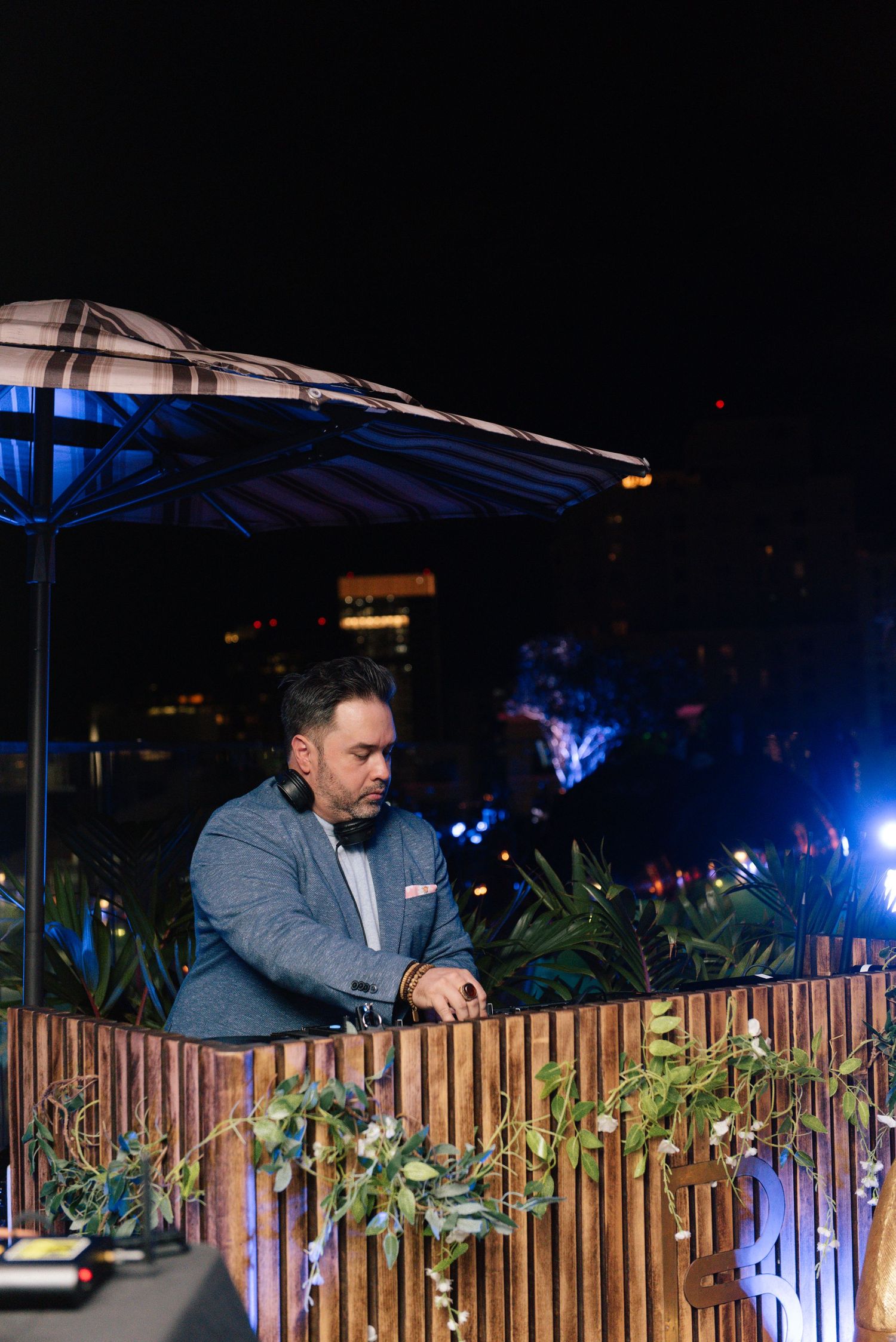 DJ booth setup with wooden slat design and tropical plants illuminated by blue lighting.