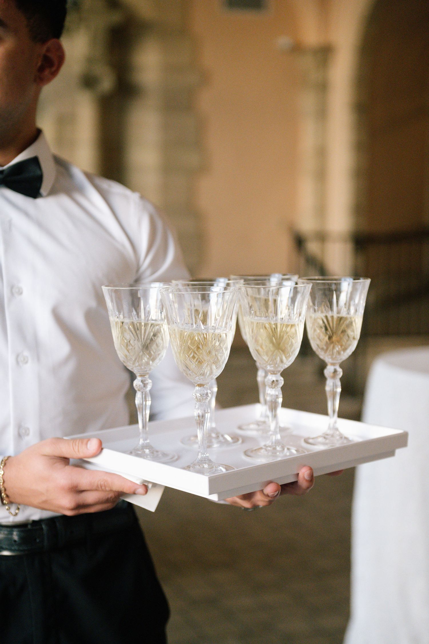 Server carrying crystal champagne glasses on silver tray at wedding reception.