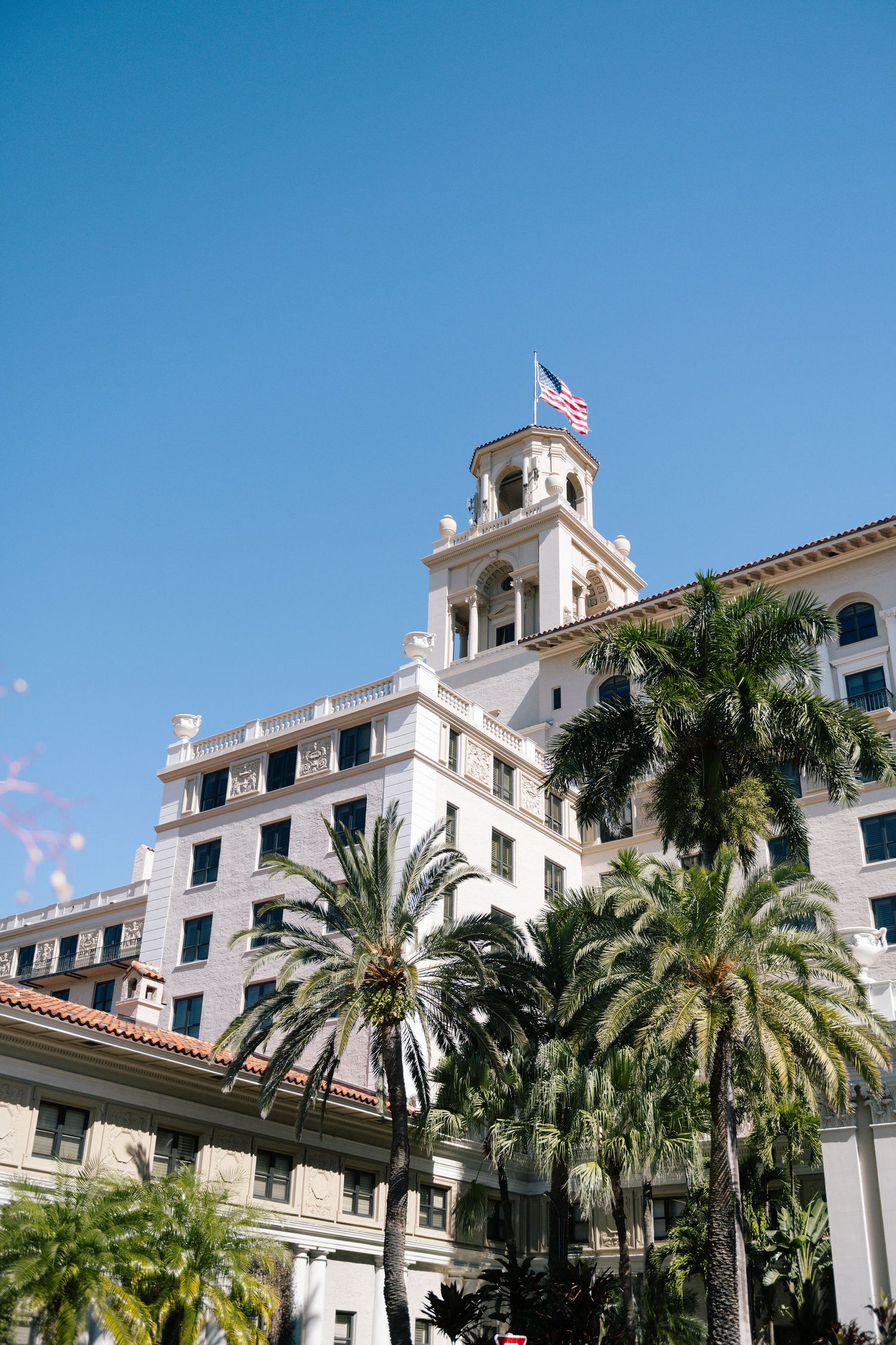 A grand white Spanish-style hotel with palm trees and blue sky in Florida.