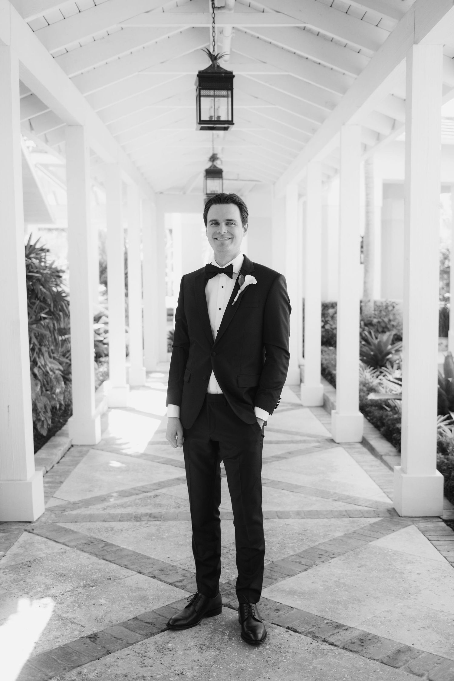 Classic black tuxedo wedding portrait in an elegant white colonnade hallway.