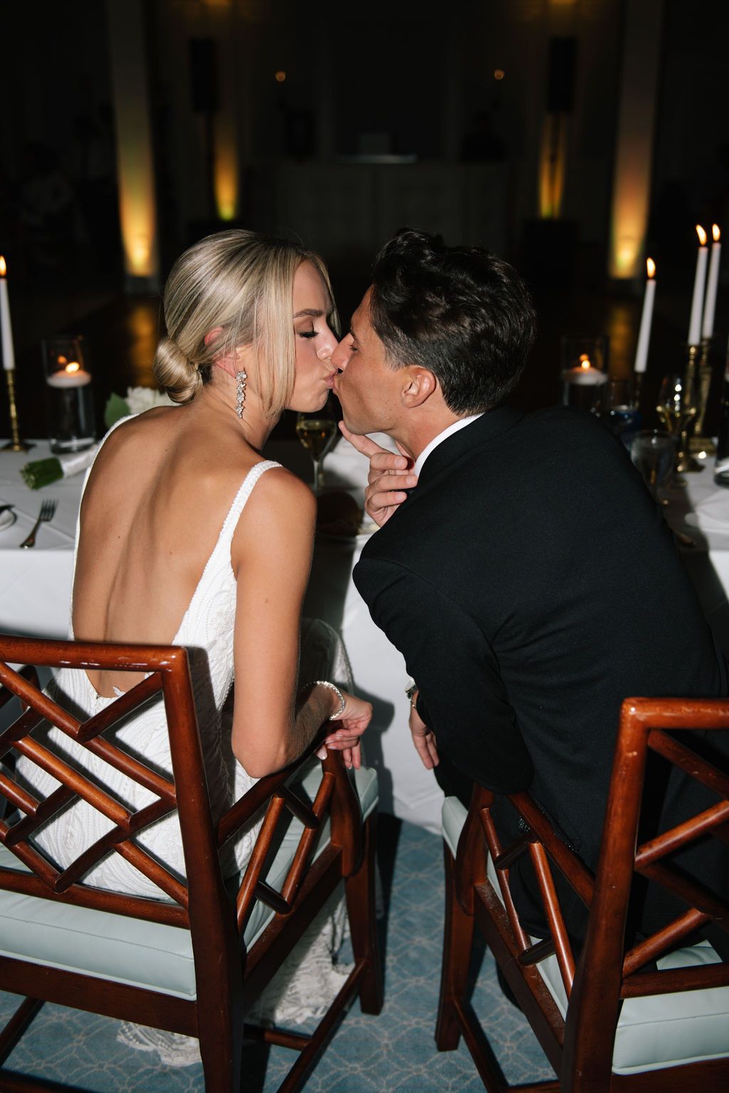 Romantic kiss shared at candlelit wedding reception dinner table.