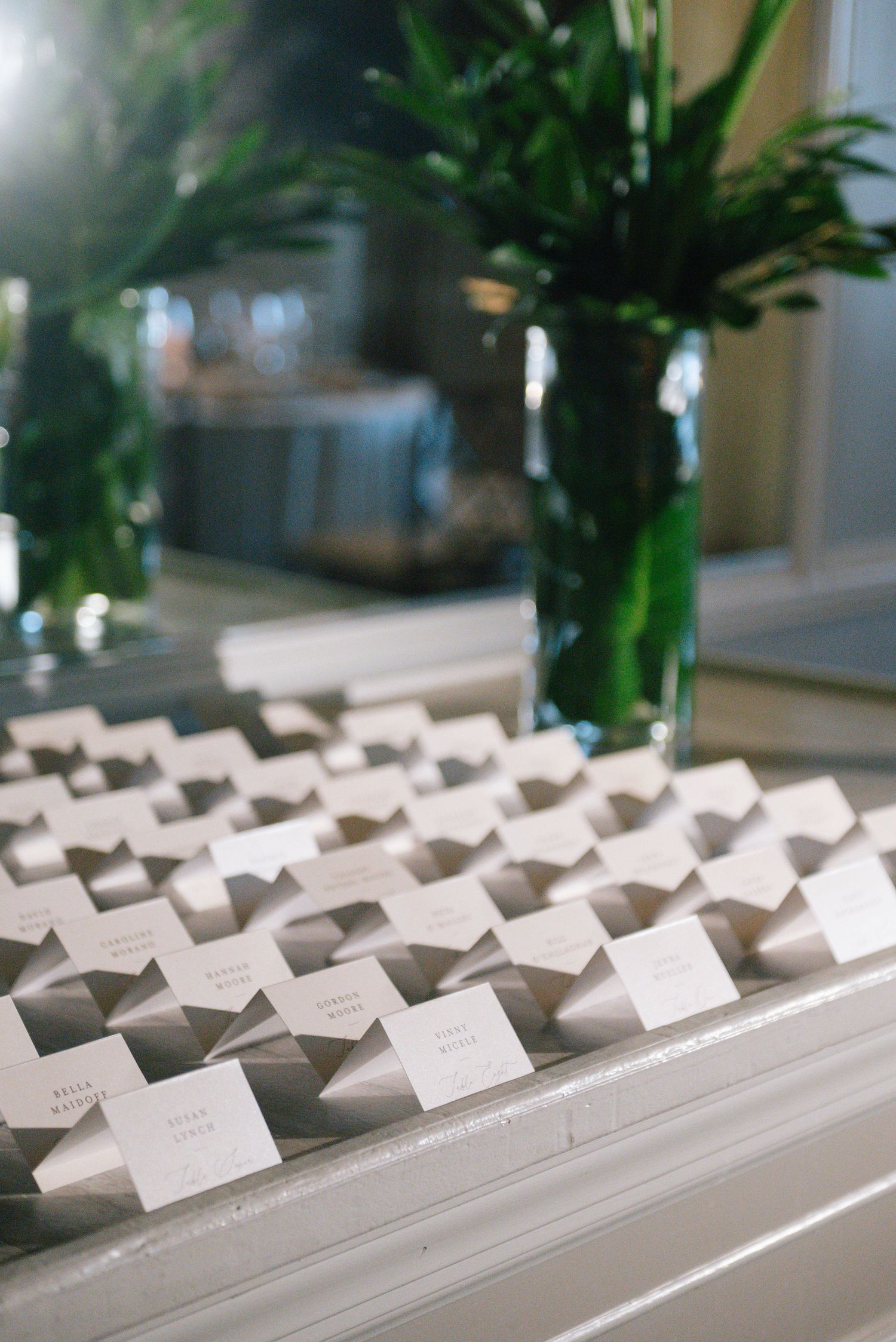 Rows of white place cards arranged neatly on a table with green floral centerpieces.