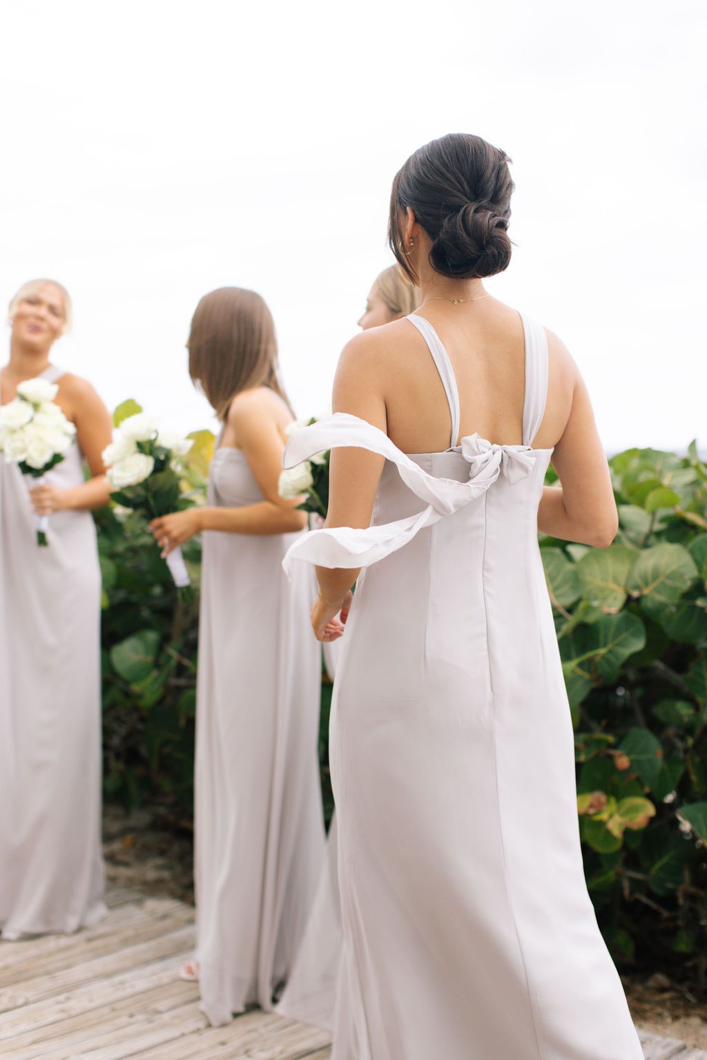 Back view of bridesmaids in matching light gray dresses standing in a row outdoors.