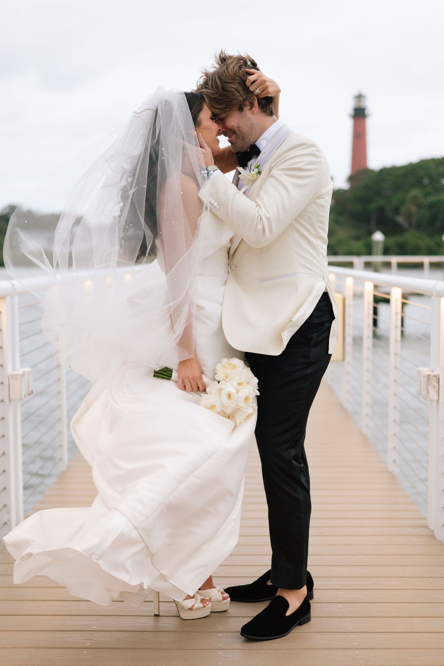 Bride and groom share playful poses on wooden dock during sunset.