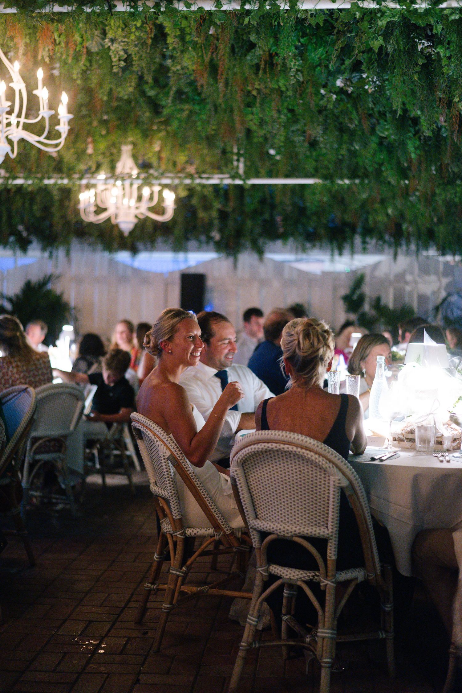 Wedding reception dinner setup under hanging greenery and chandeliers.