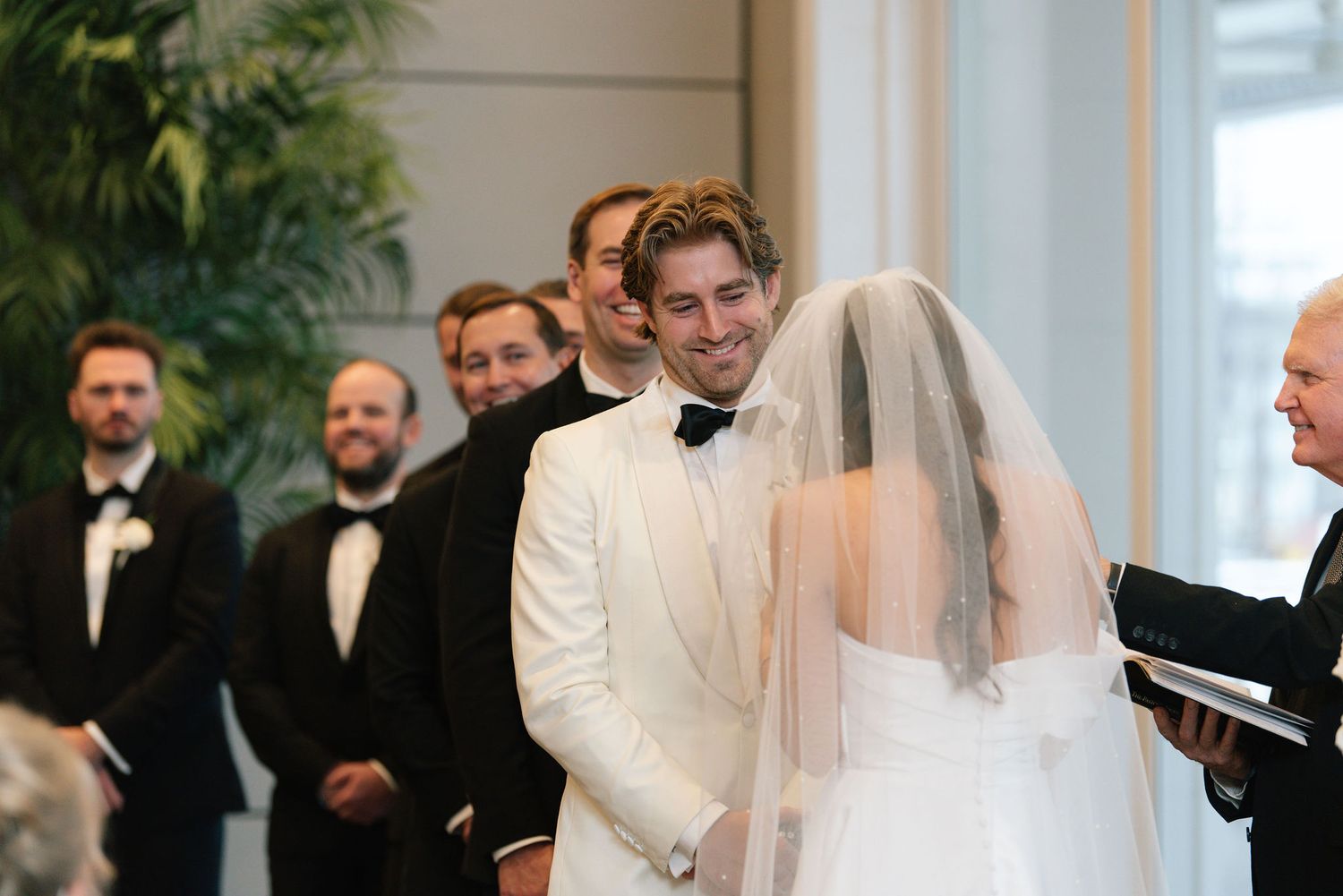 Indoor wedding ceremony with white decor and natural lighting.