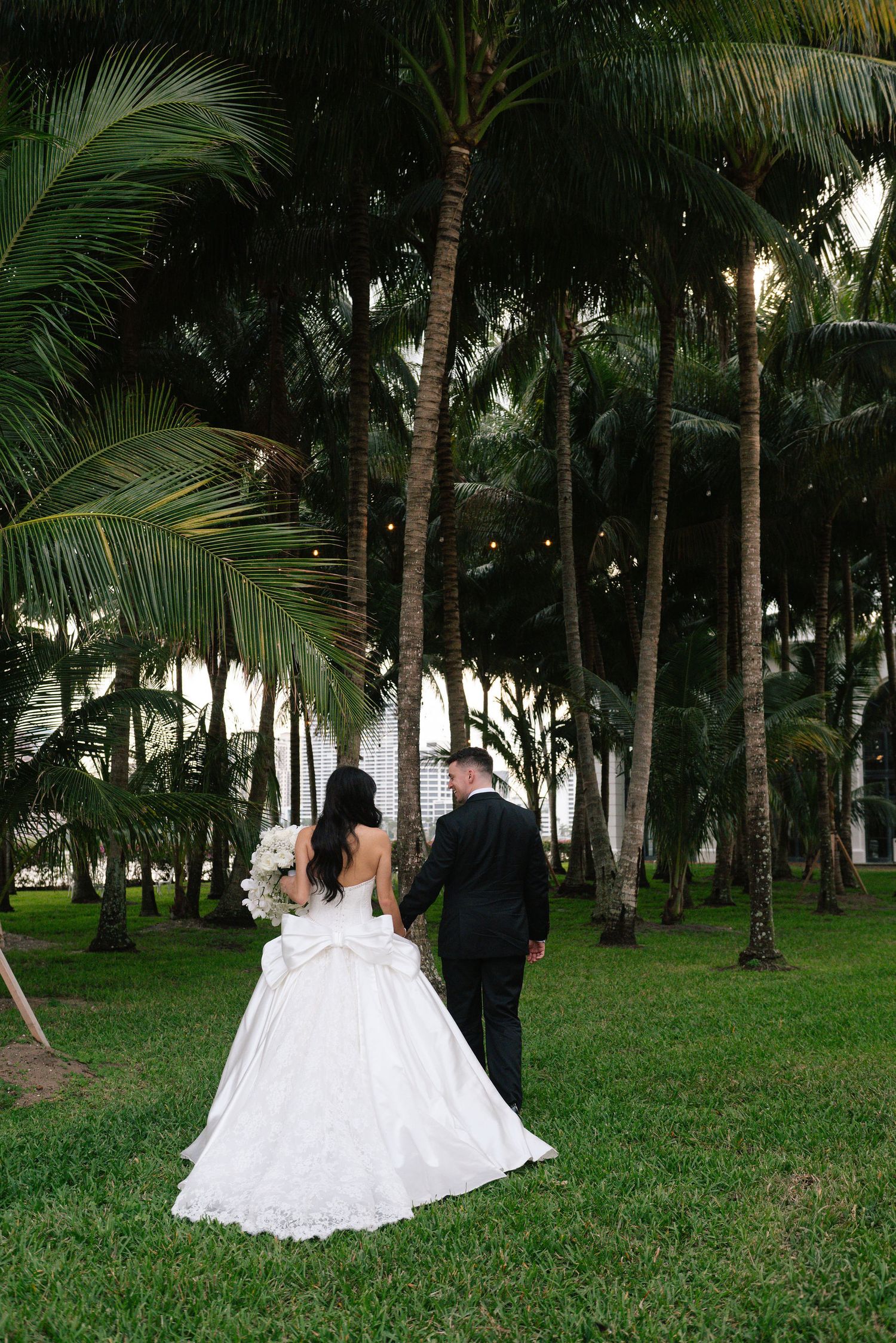 Newlyweds walk hand in hand through a tropical palm tree garden.