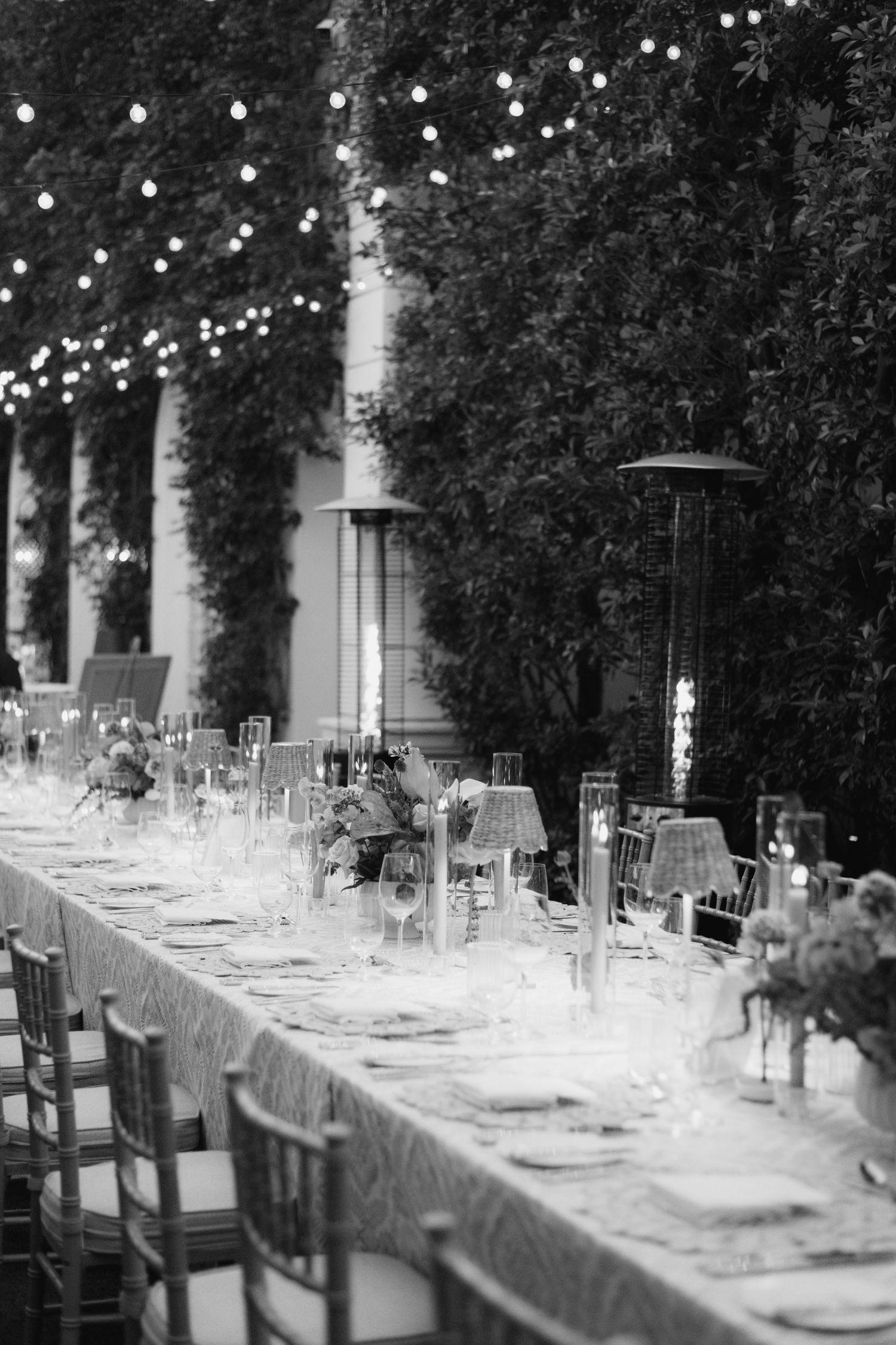 Black and white photo of an elegant outdoor wedding reception table setup with string lights and place settings.