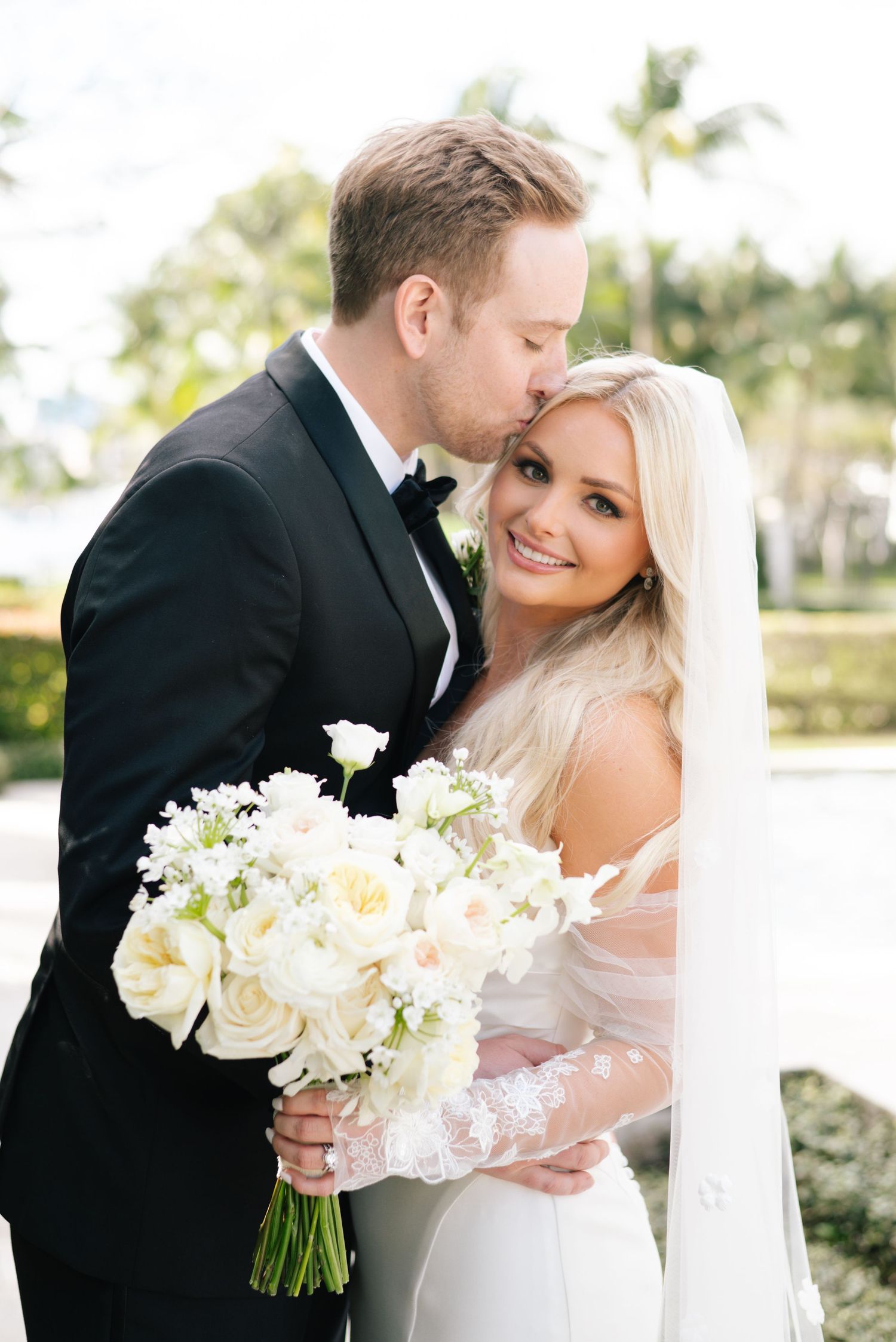 An elegant wedding couple shares intimate moments while holding a bouquet of white roses.