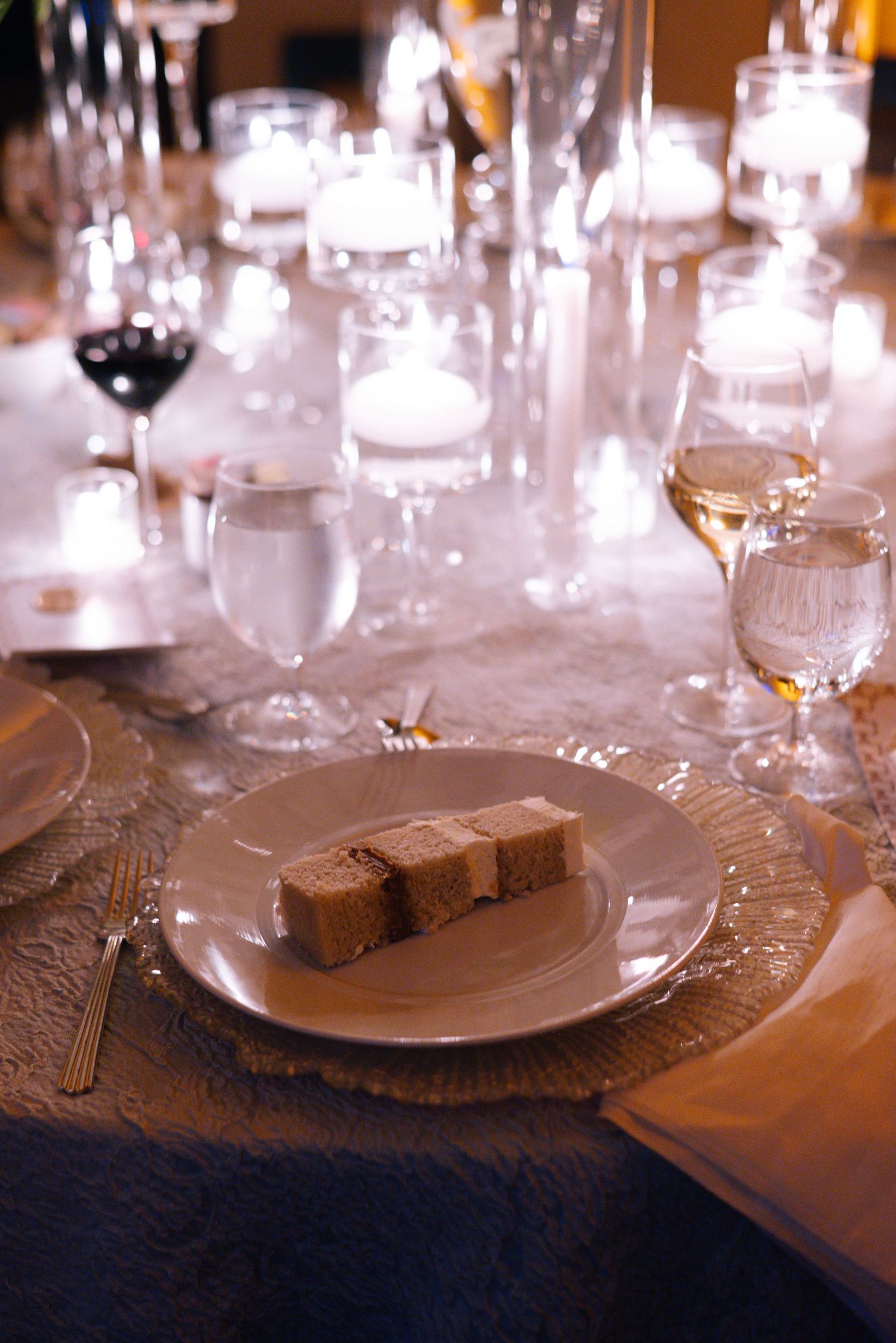 Formal dining table with crystal glasses and white plates set against a textured tablecloth in warm lighting.