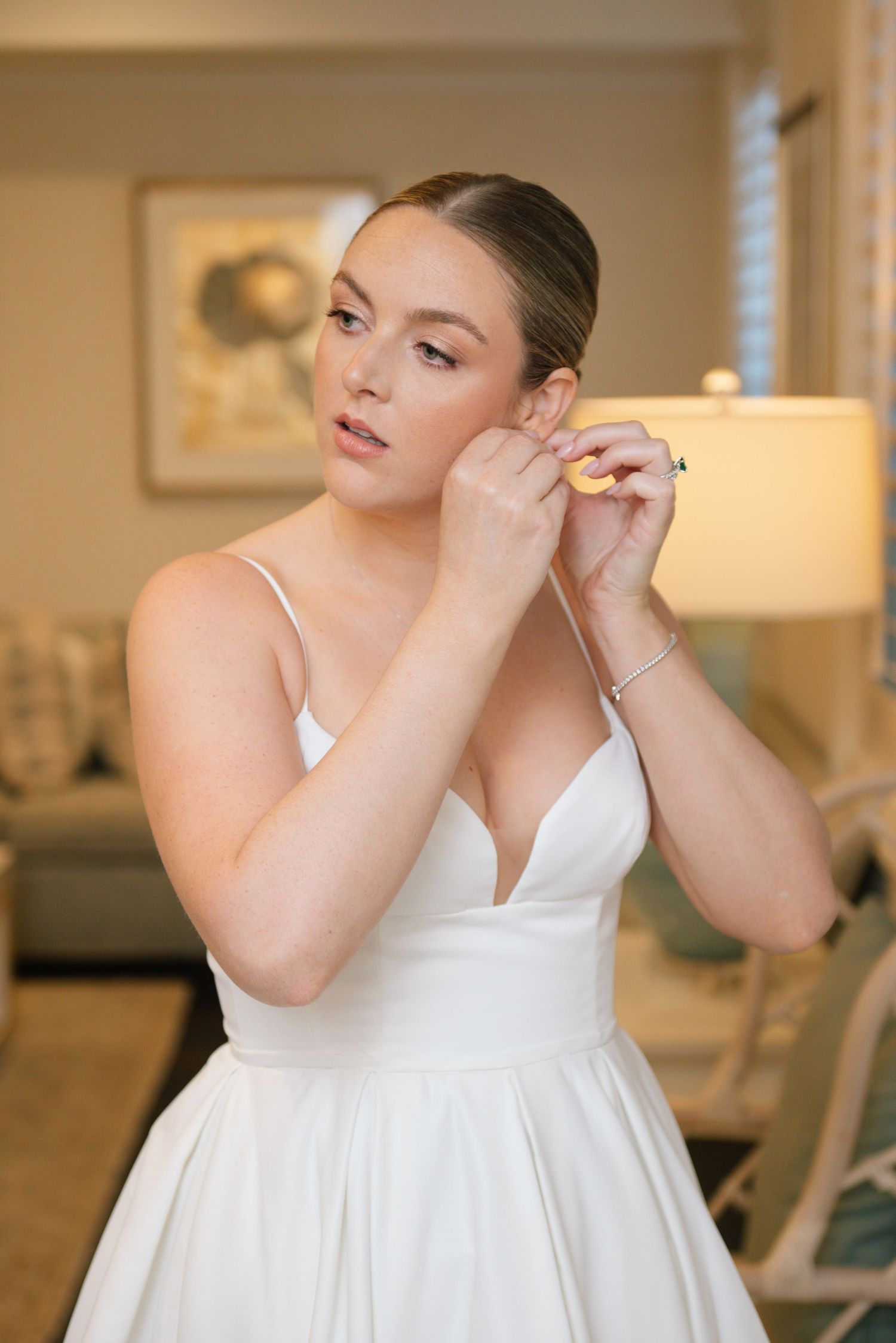 Bride in a classic white wedding dress puts on earrings while getting ready for her special day.