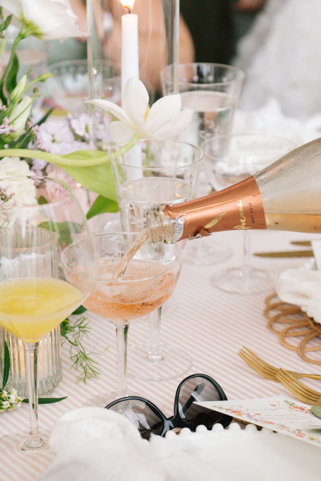 Rose champagne being poured into glasses at an elegant table setting with flowers and candles.