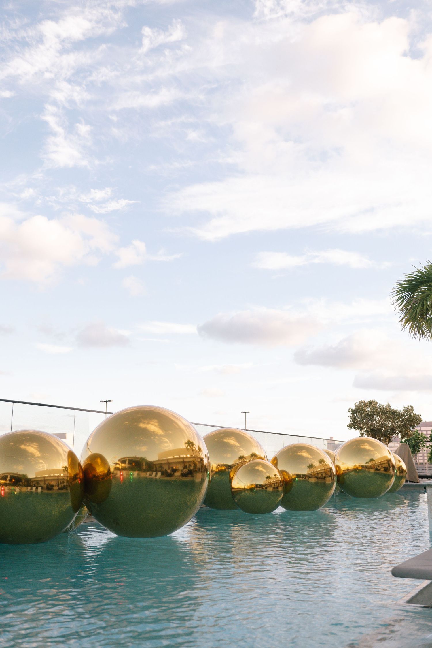 Row of large golden reflective spheres floating on water during sunset.
