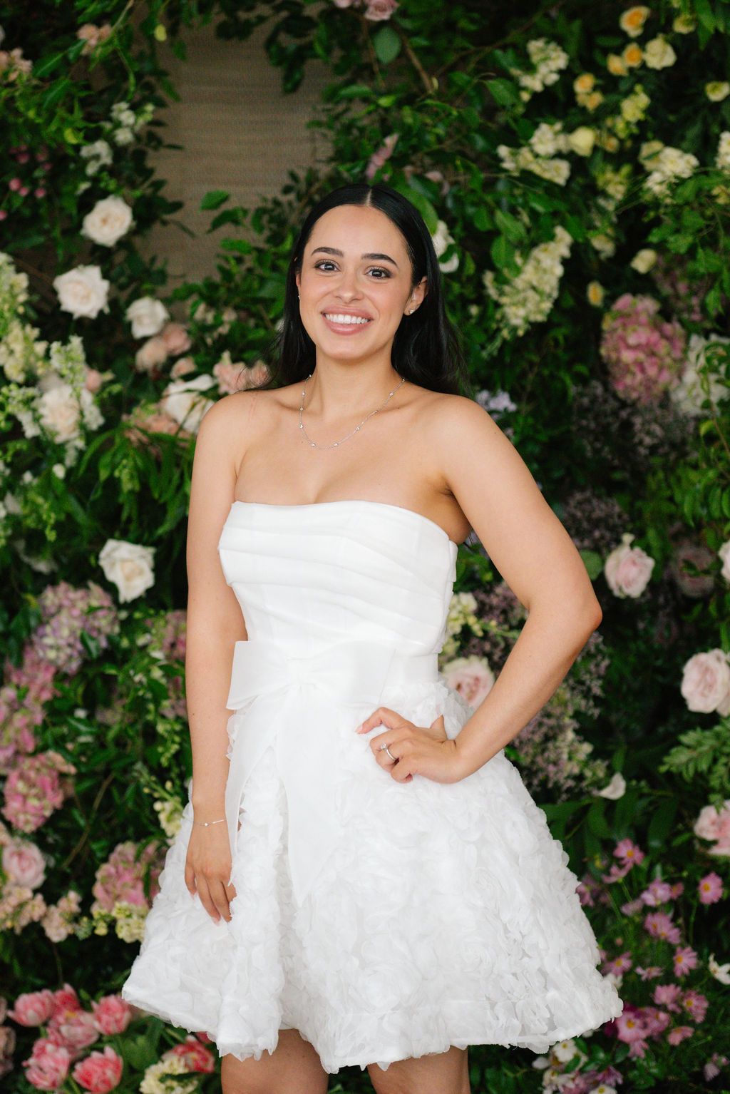 A short white wedding dress portrait session with pink roses and greenery in the background.
