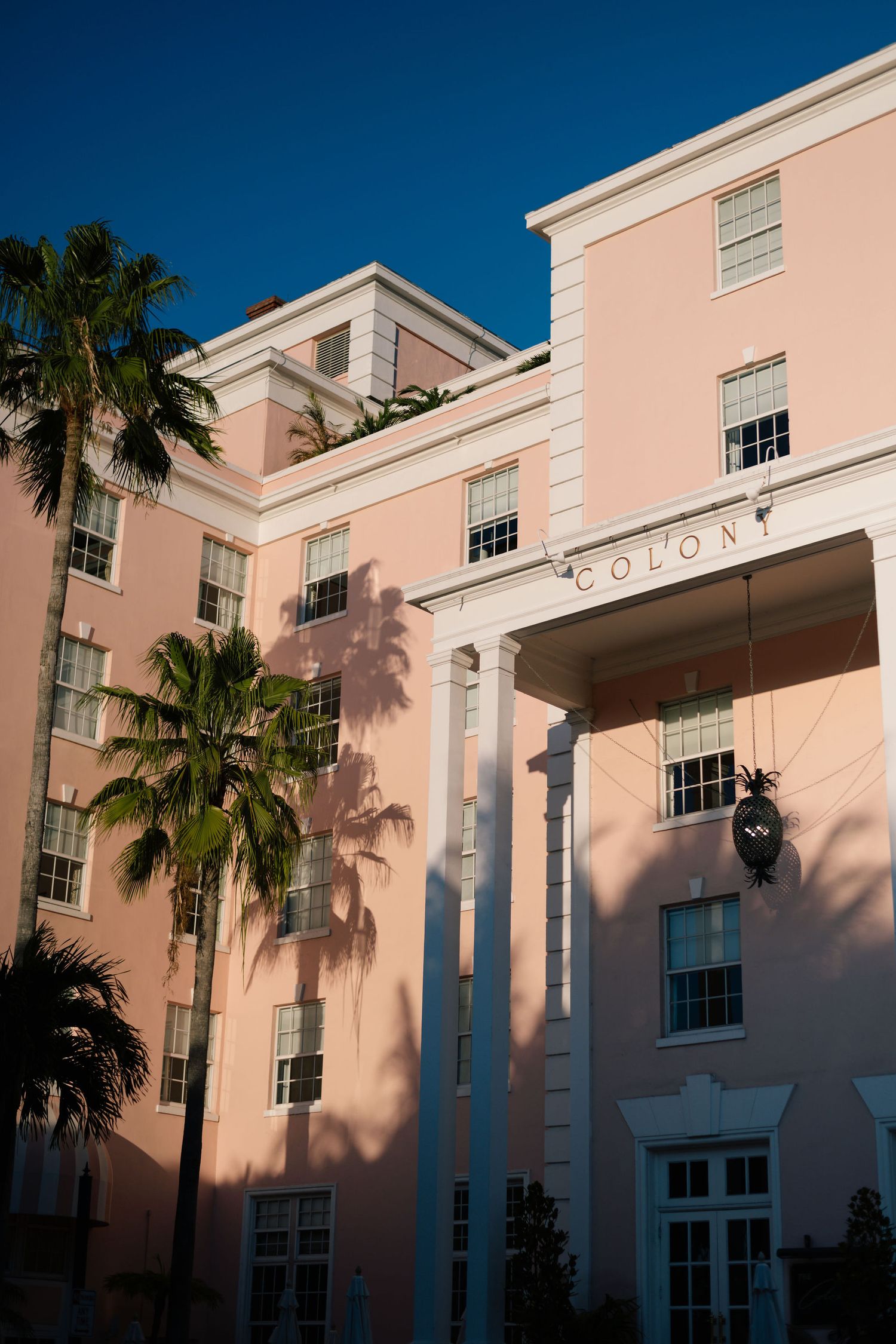 Pink colonial-style building with white trim and palm trees against bright blue sky.