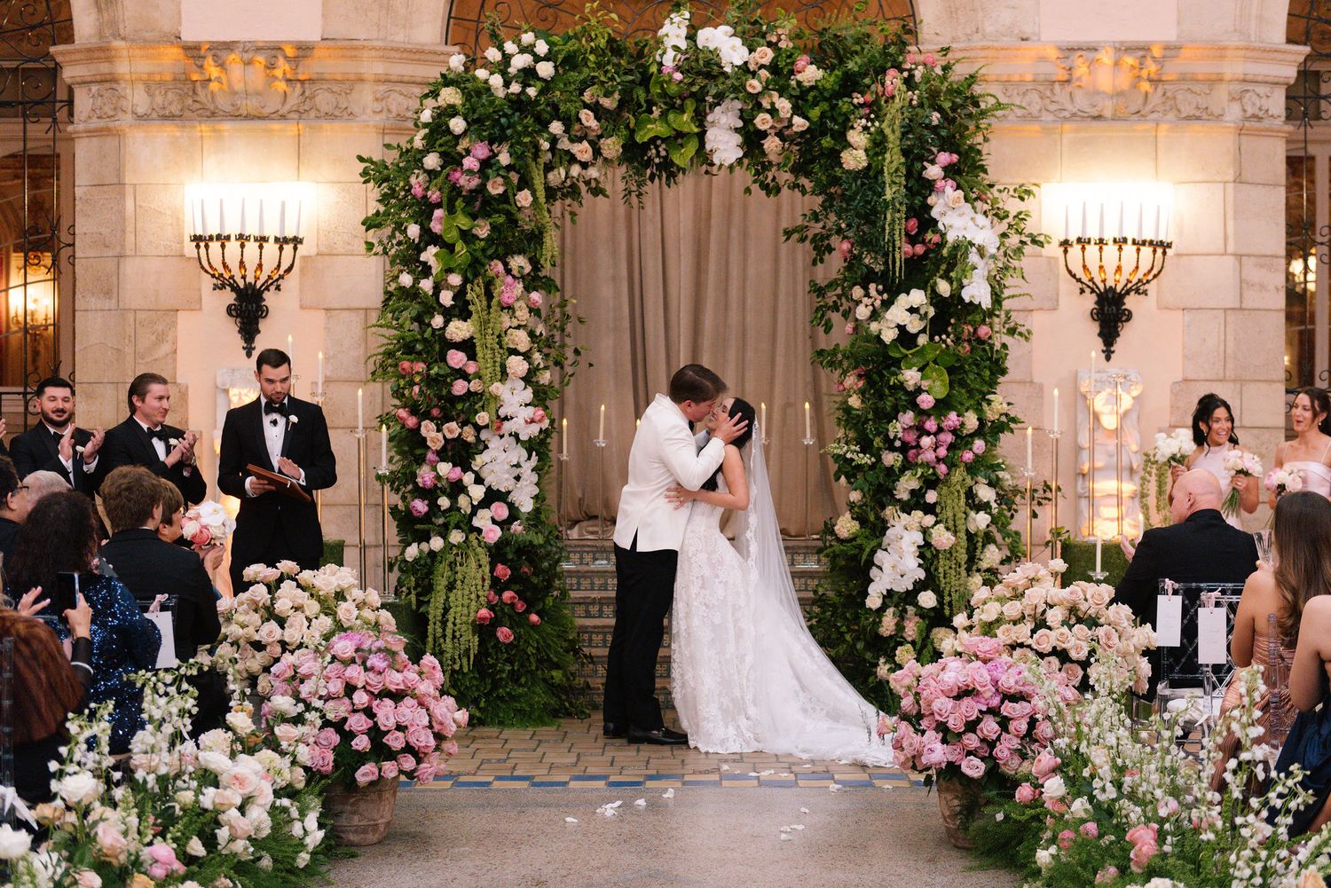 Wedding ceremony in progress with romantic floral arch decorations and soft lighting.