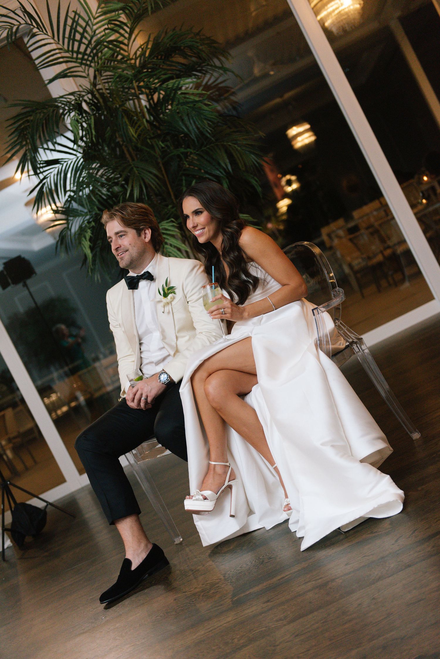 A couple sits together on a wooden dance floor with tropical plants decorating the venue.