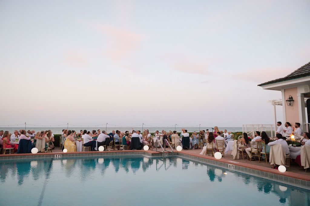 Panoramic view of a poolside wedding reception during sunset with guests seated at tables.