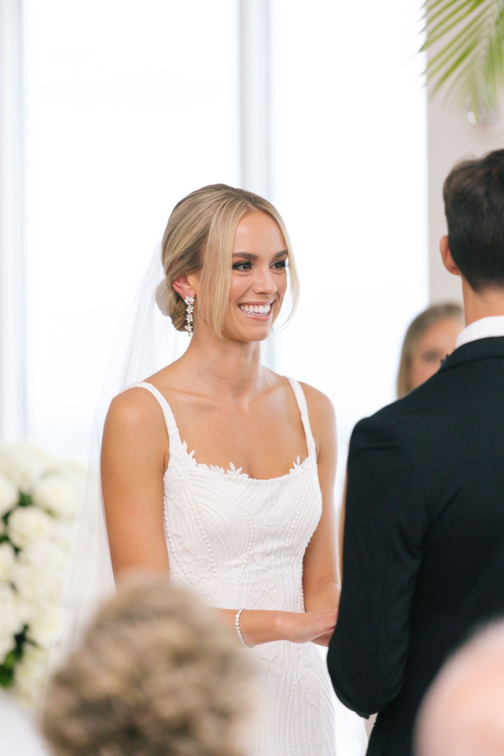 Bride in white lace dress exchanging vows during indoor wedding ceremony.