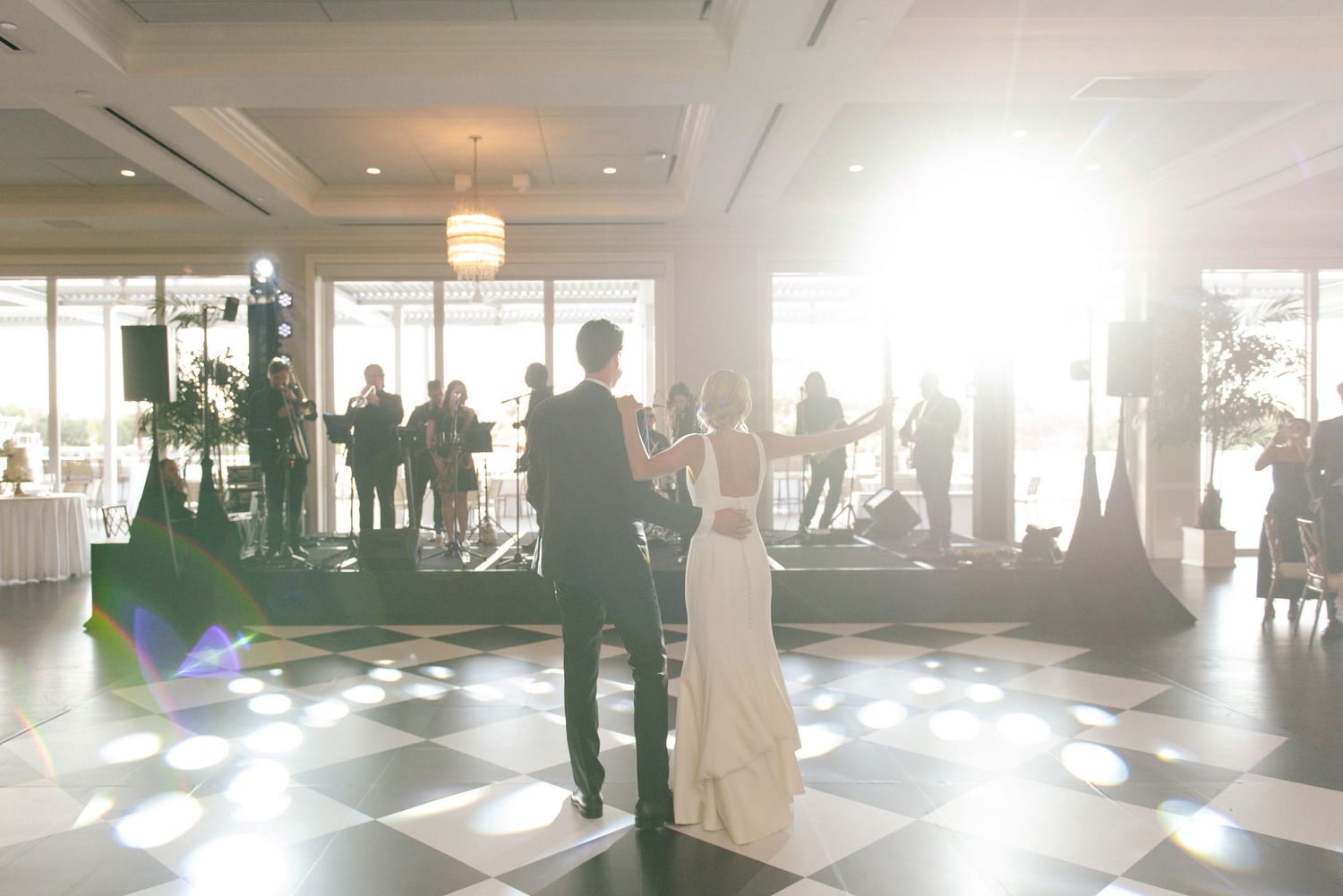 Wedding guests mingle in an elegant reception venue with white decor and natural lighting.