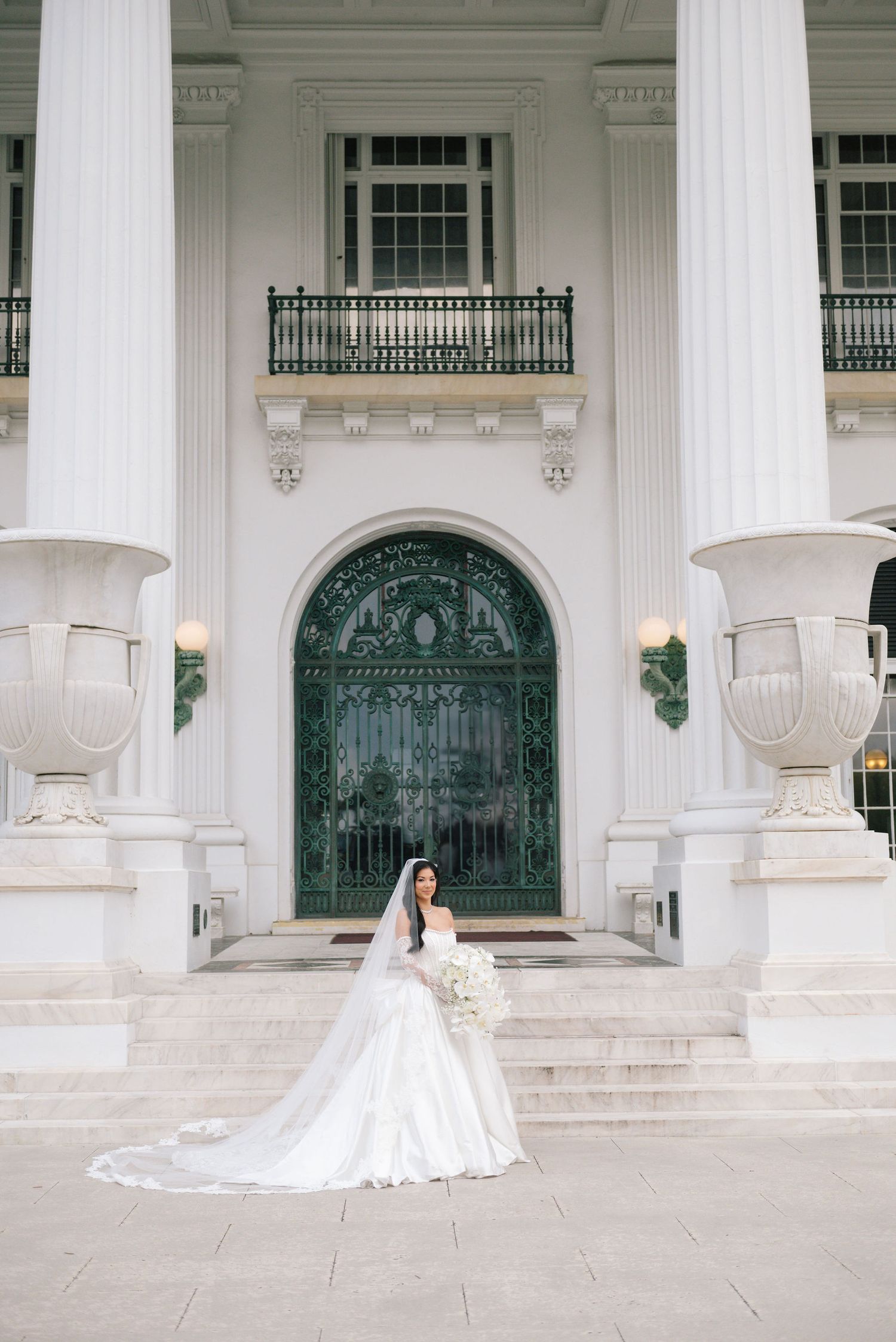 A wedding photo featuring ornate white columns and decorative green doors in classical architecture.