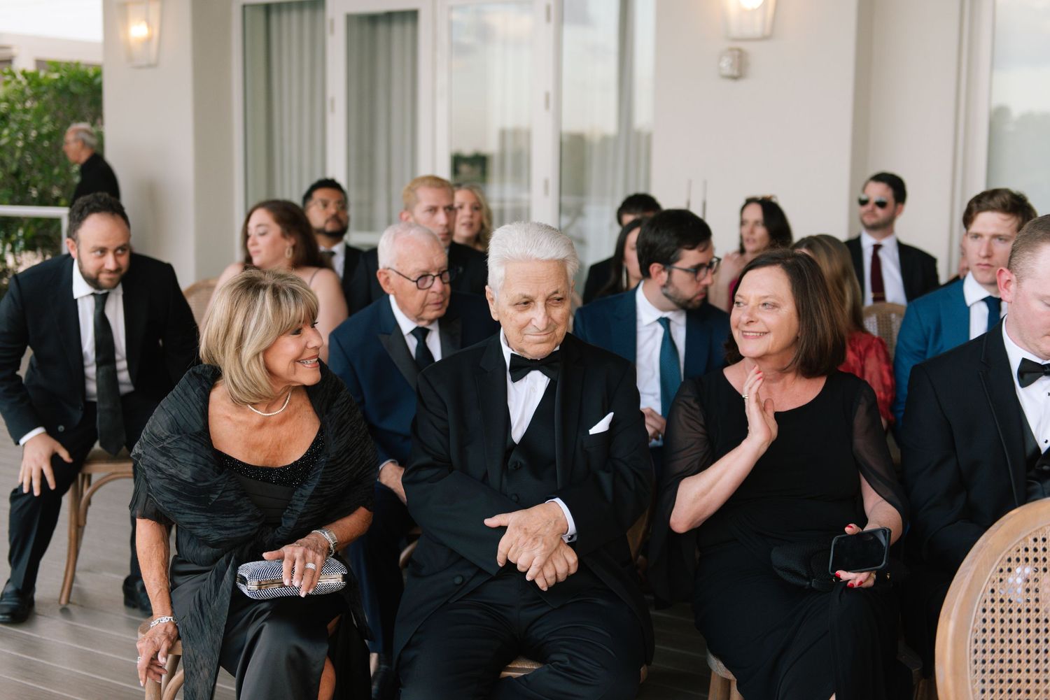 Wedding guests in formal attire enjoying a celebration in an elegant white room.