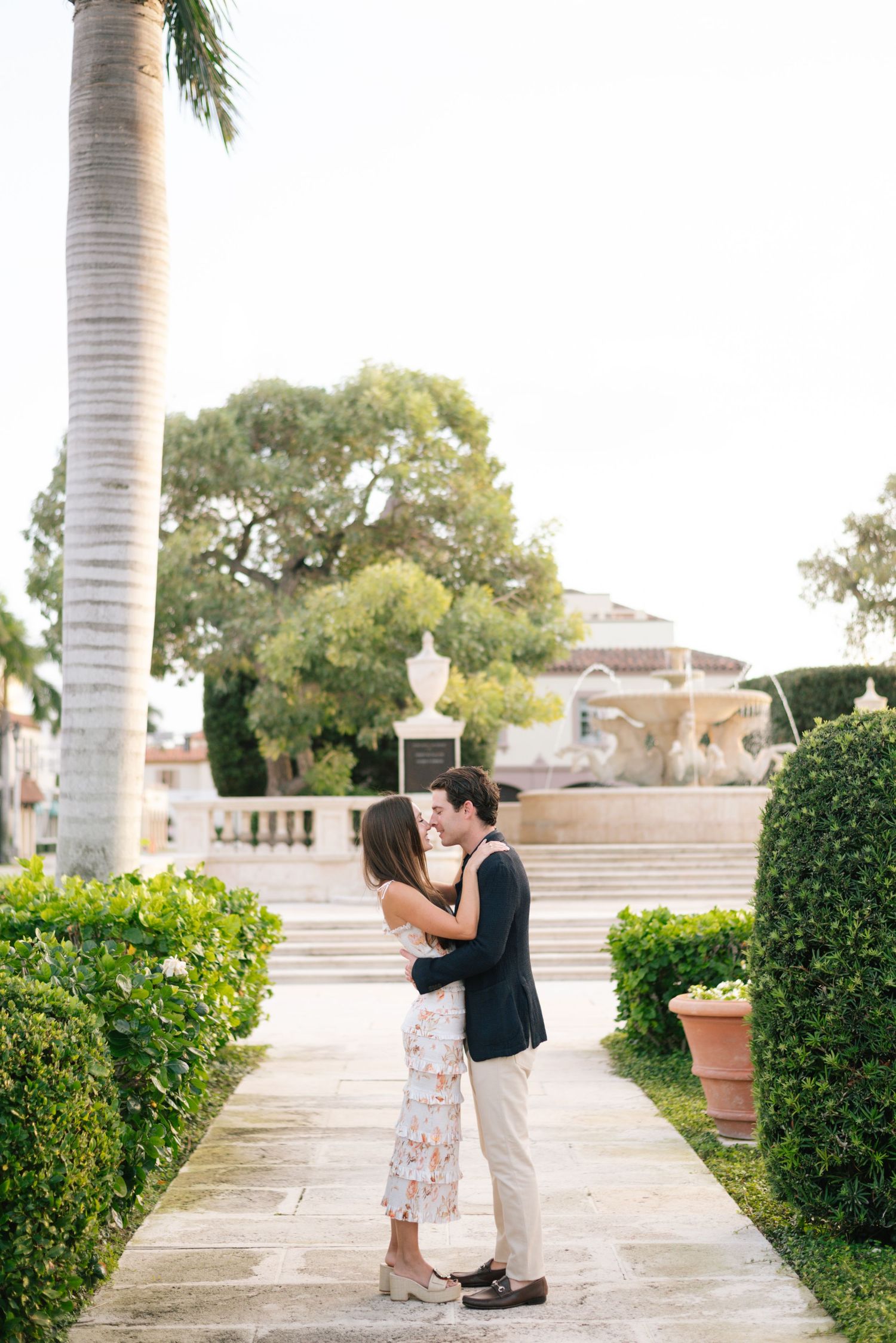 A romantic moment captured on a garden pathway with palm trees and manicured hedges at a luxurious estate.
