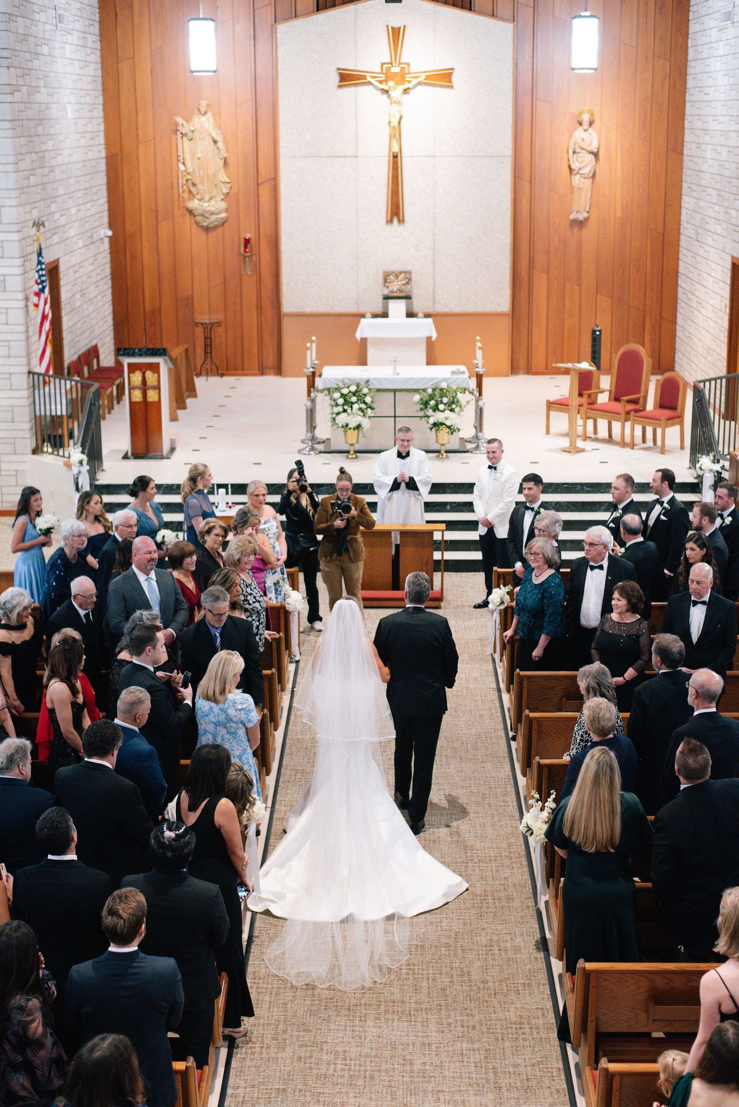A traditional Catholic church wedding ceremony with guests seated in wooden pews and a crucifix on the altar.