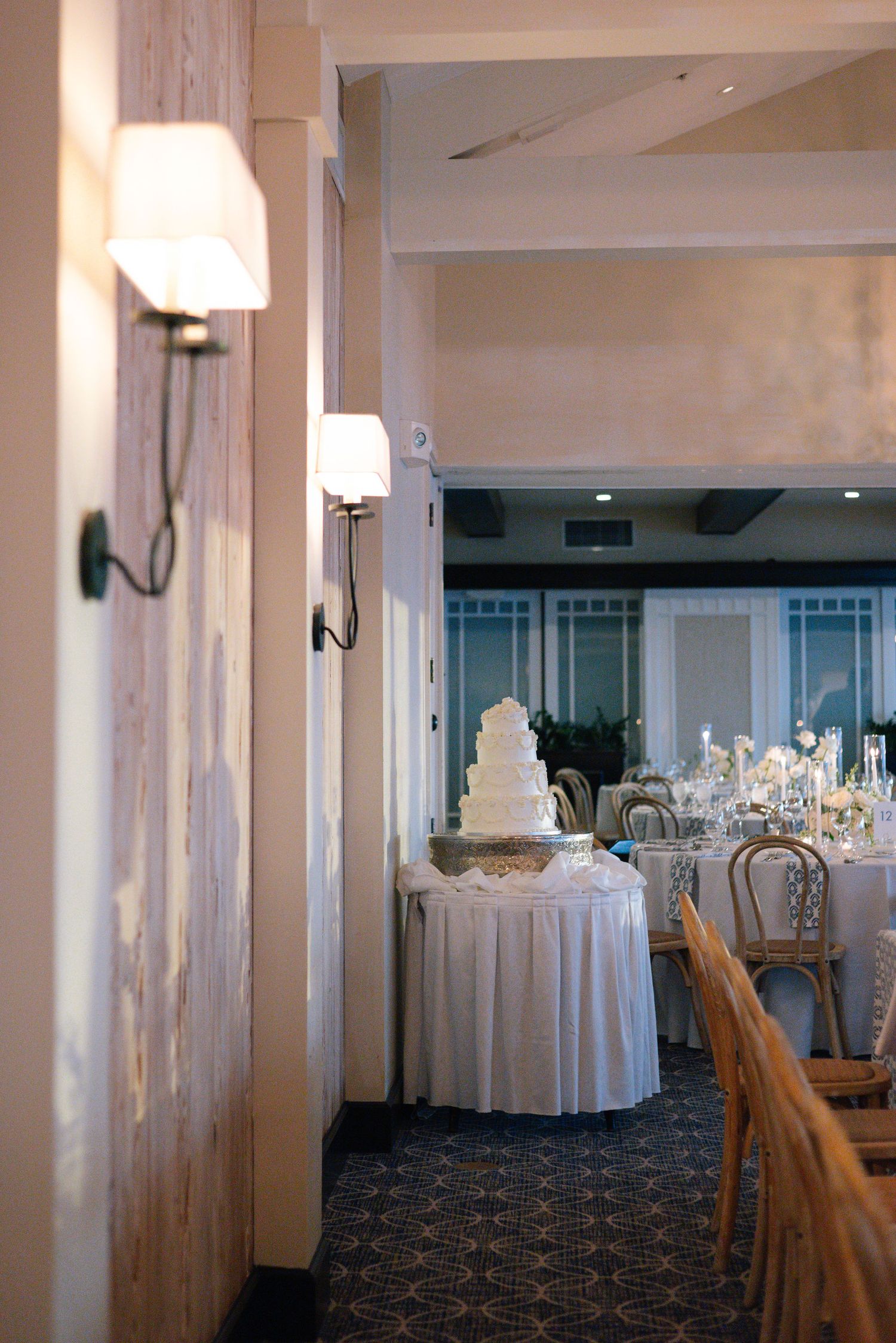Empty wedding reception venue with white draped tables and chairs arranged around a carpeted ballroom.