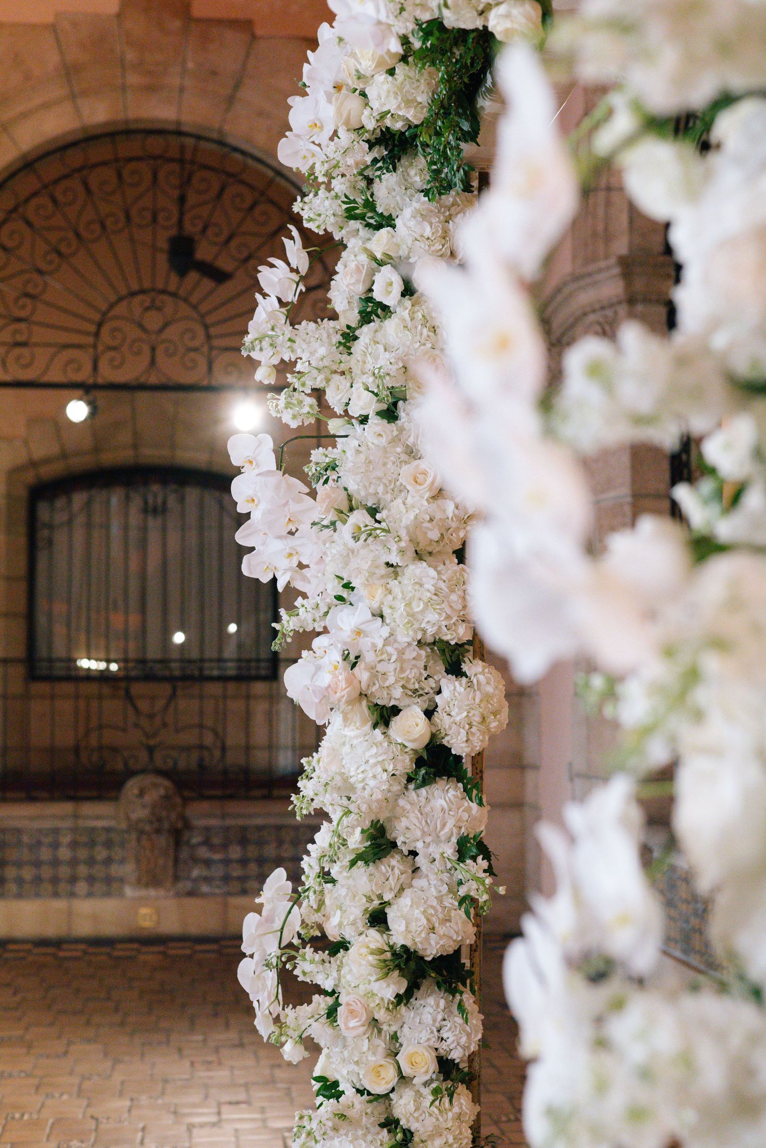 Stunning white floral arch covered in roses and orchids at elegant wedding venue.