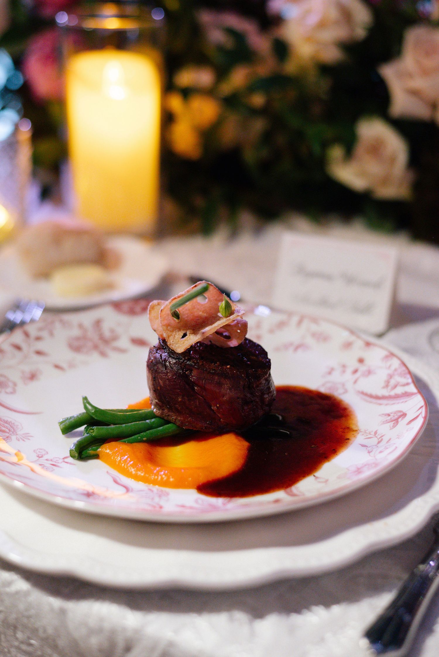 Gourmet plated dinner with beef tenderloin, vegetables, and sauce on decorative china.