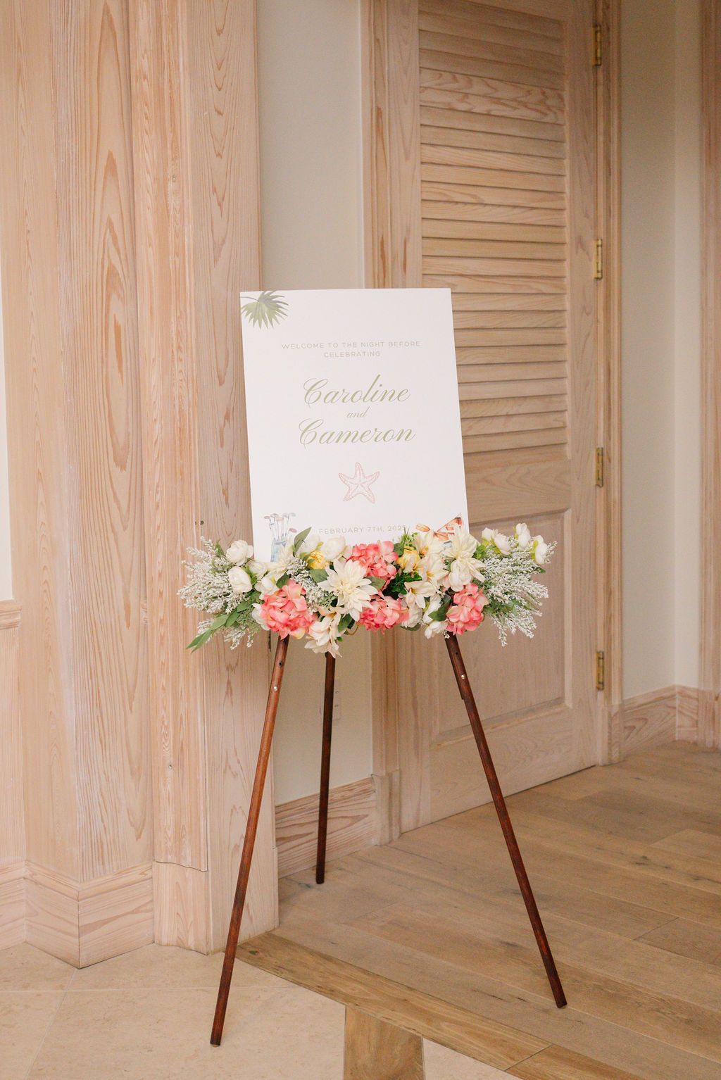 Elegant wedding welcome sign with pink floral arrangement on wooden easel.