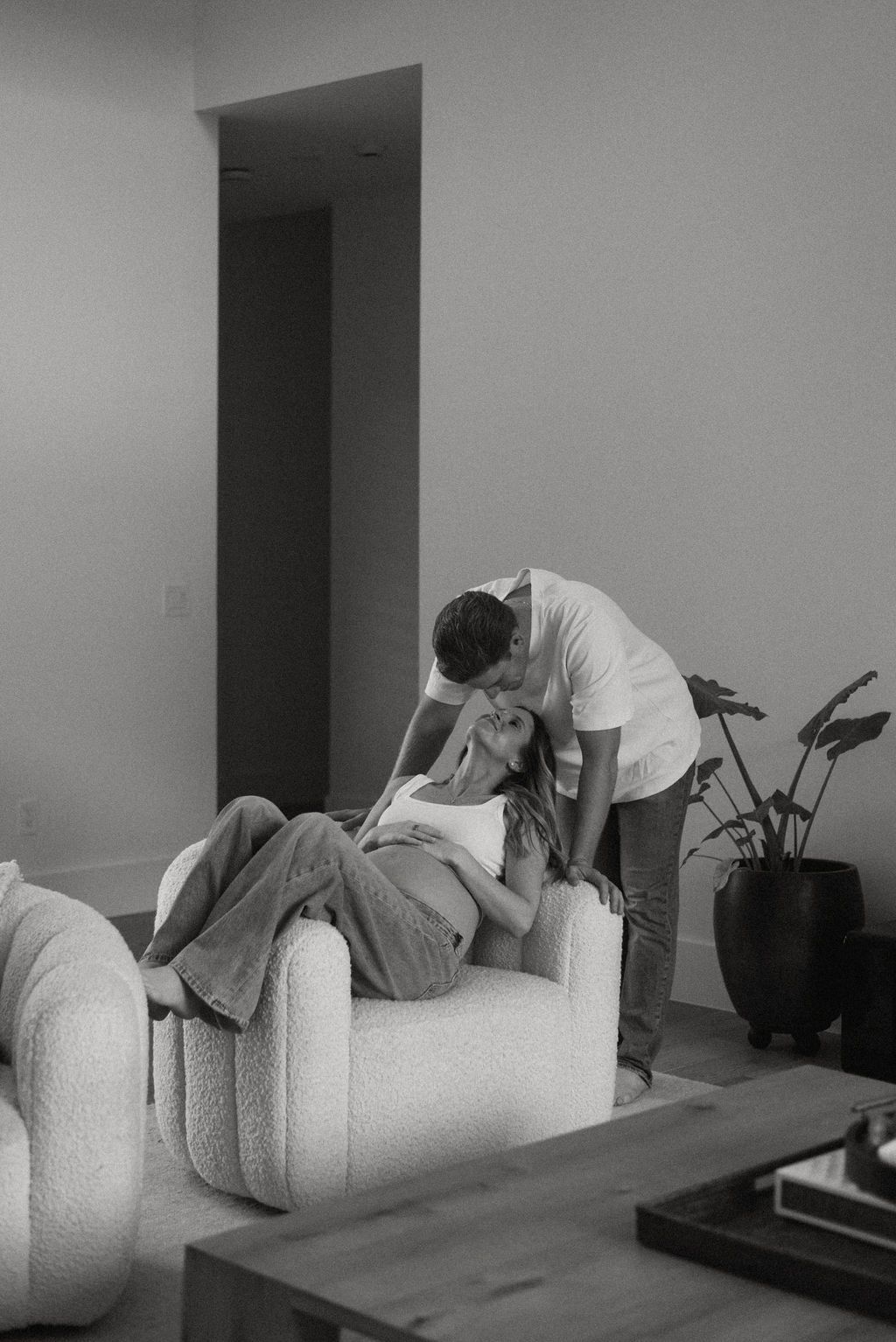 A couple relaxes together on a white couch during an intimate indoor photoshoot.
