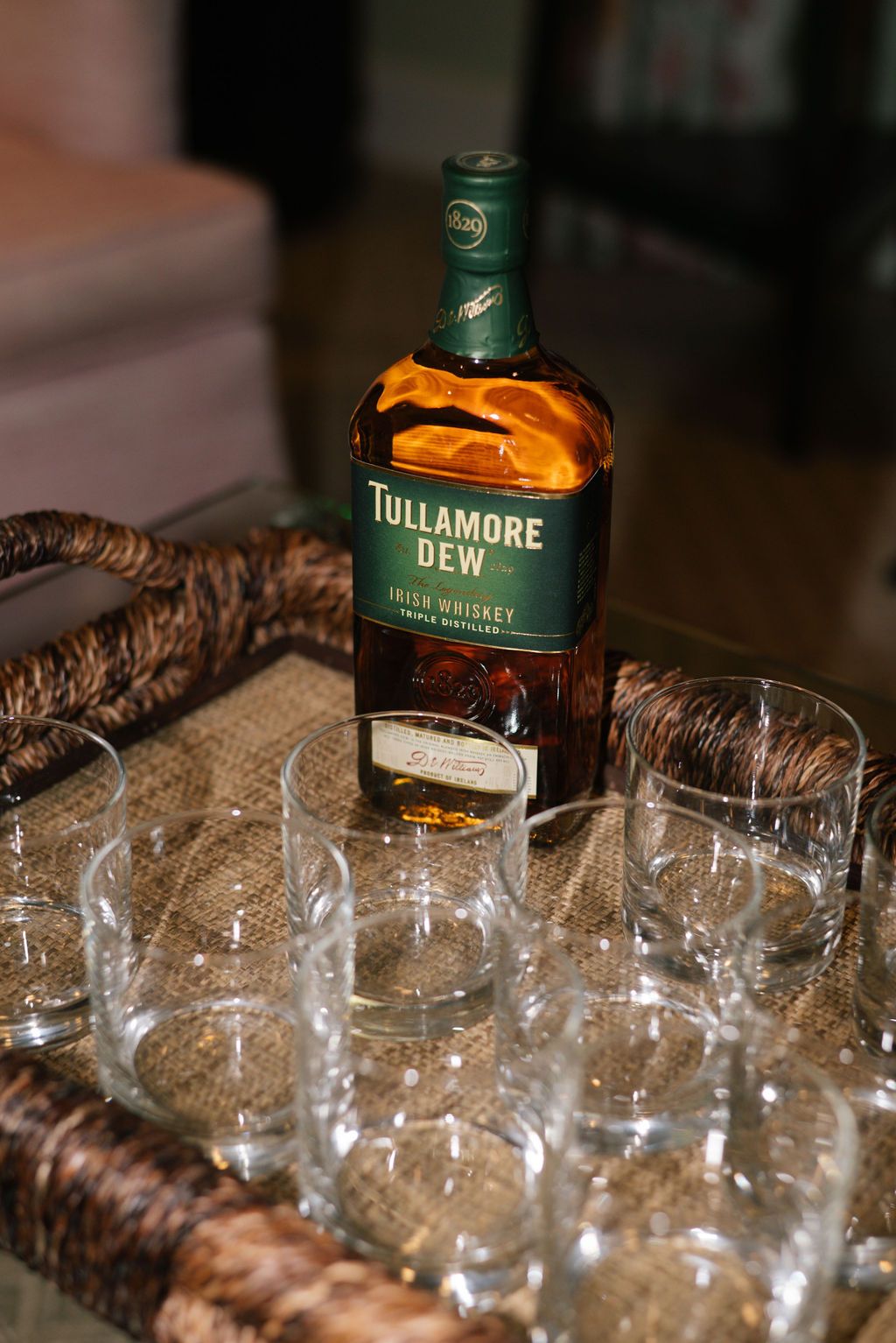 Bottle of Tullamore Dew Irish whiskey with empty glasses arranged on woven tray.