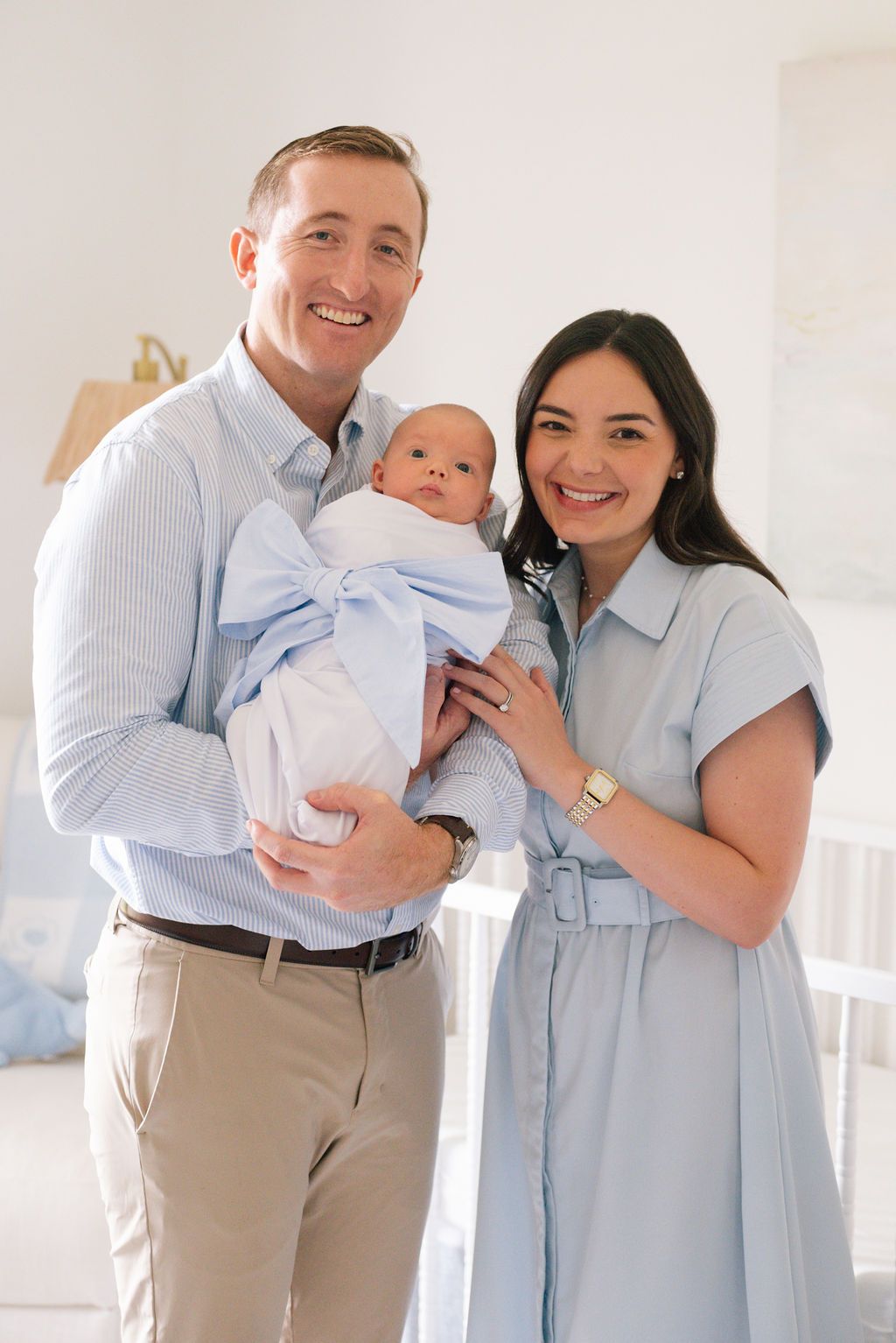 A couple in light blue and khaki outfits share tender moments with their baby in a bright indoor setting.
