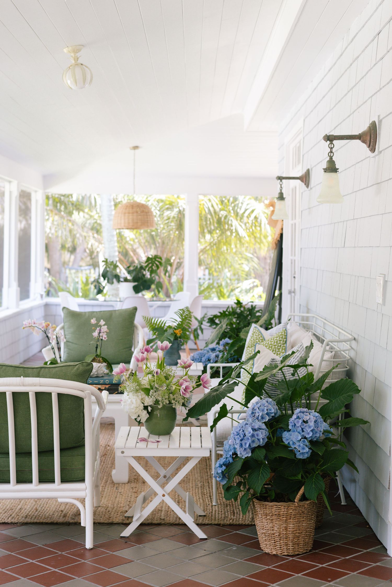Coastal porch decorated with green cushions, woven furniture, and fresh hydrangea arrangements.