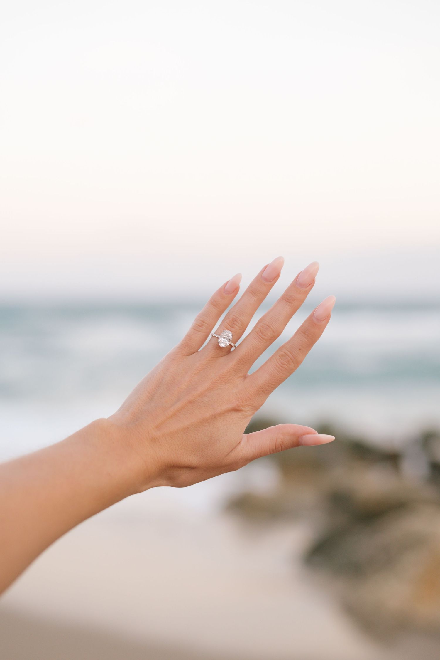 Close-up shots of an elegant diamond engagement ring on a woman's hand with ocean waves in background.