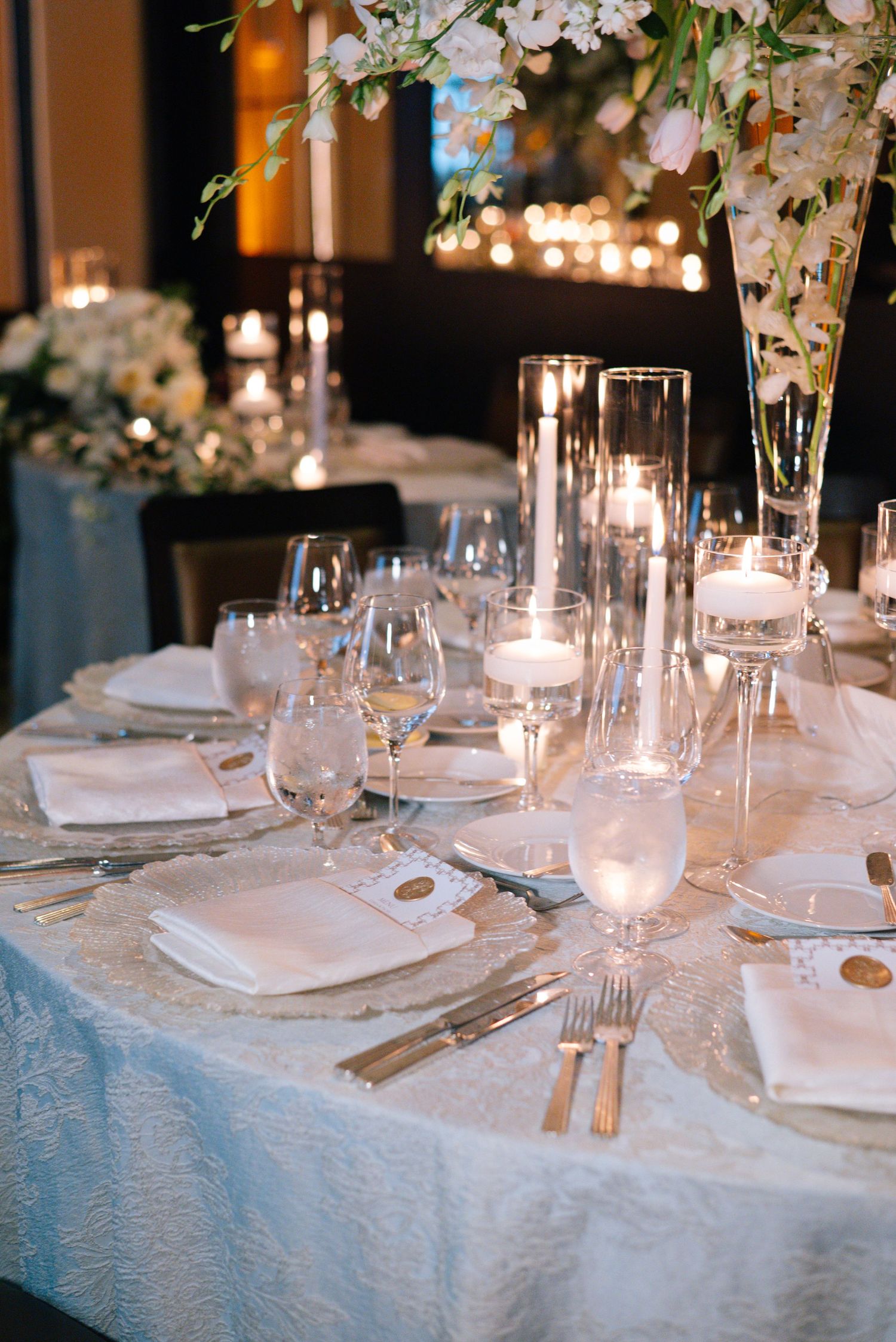 Elegant table setting with white linens, crystal glassware, and delicate floral arrangements for a formal dining event.